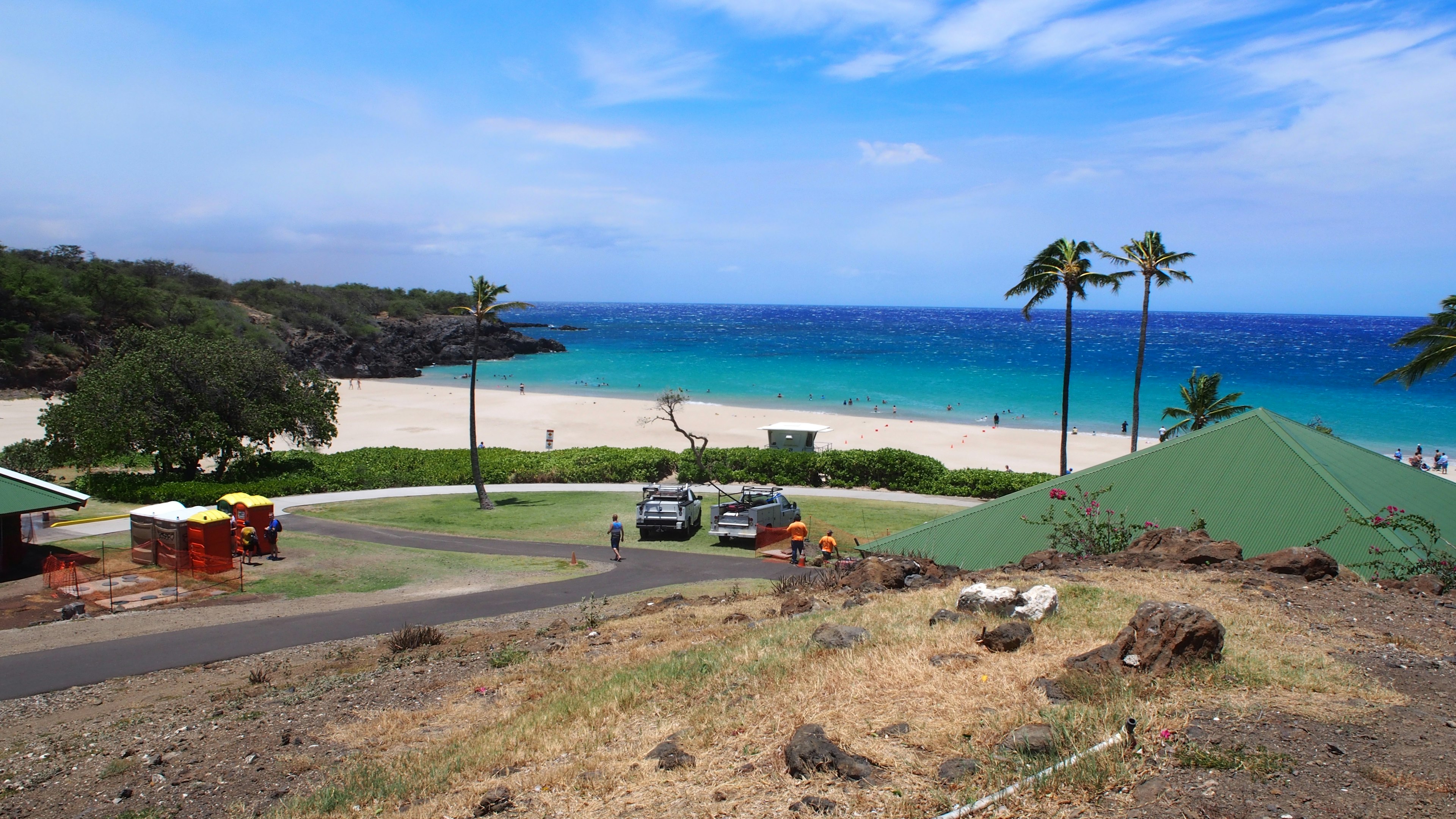 Vista escénica de una playa con océano azul y arena blanca, palmeras a lo largo de la costa y personas a lo lejos