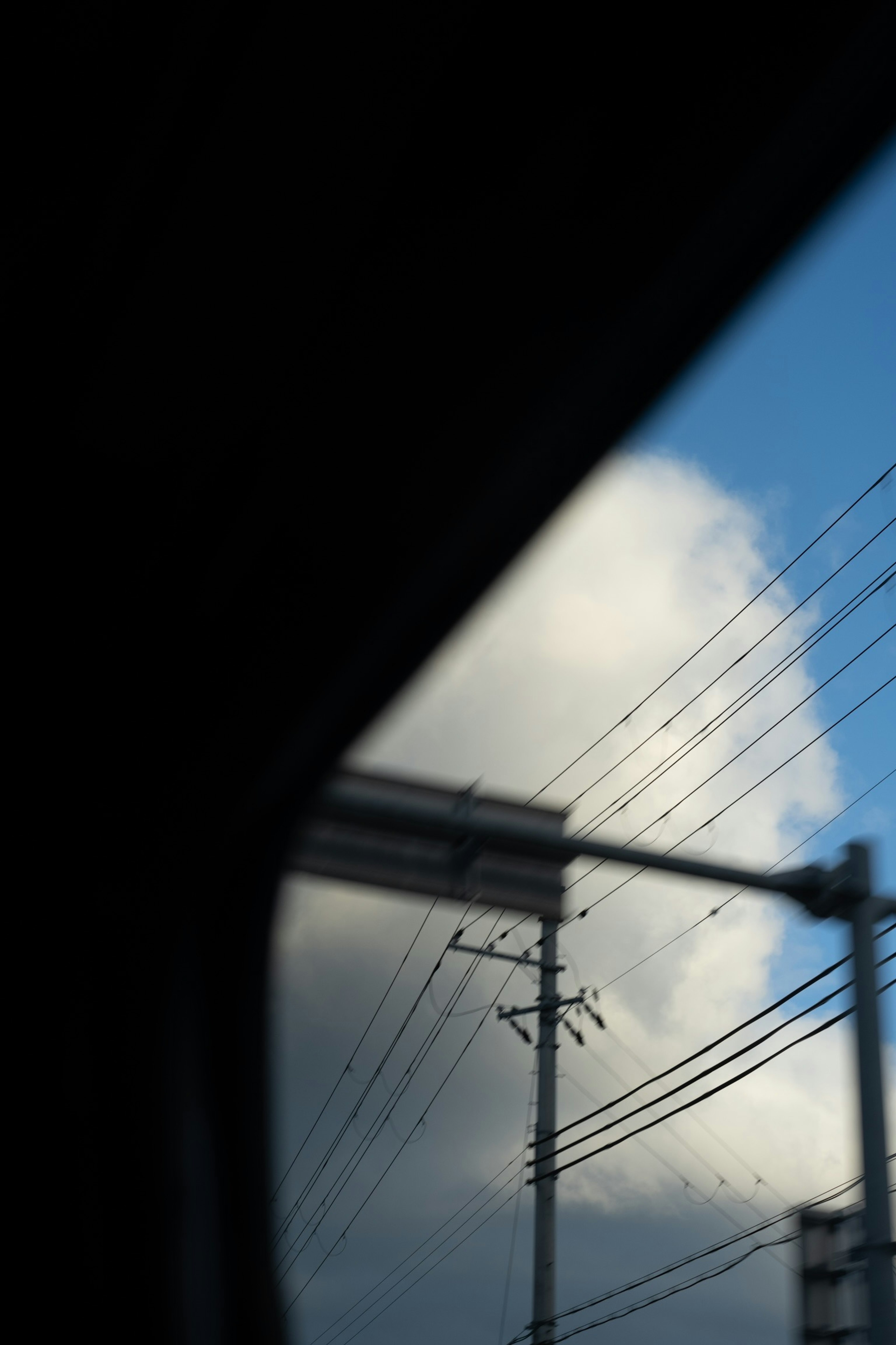 Vue depuis une fenêtre de voiture montrant un ciel bleu et des nuages blancs avec des lignes et des poteaux électriques