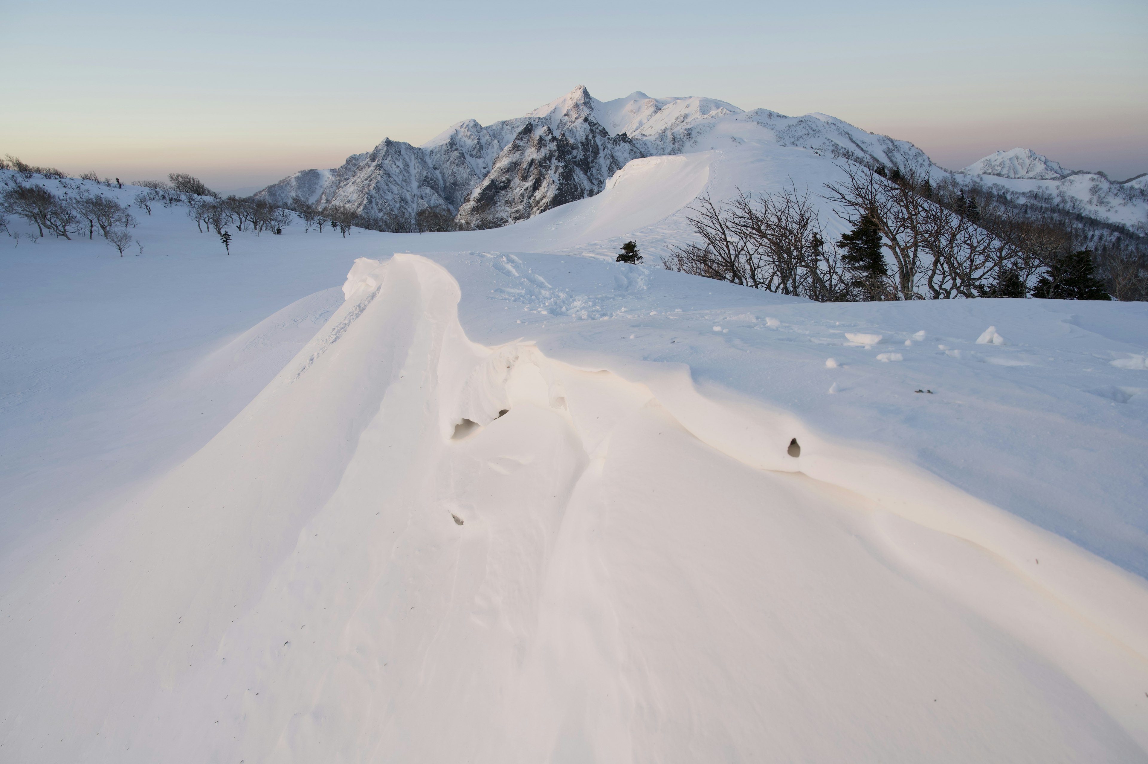 Paisaje montañoso cubierto de nieve con picos majestuosos y cielo al atardecer