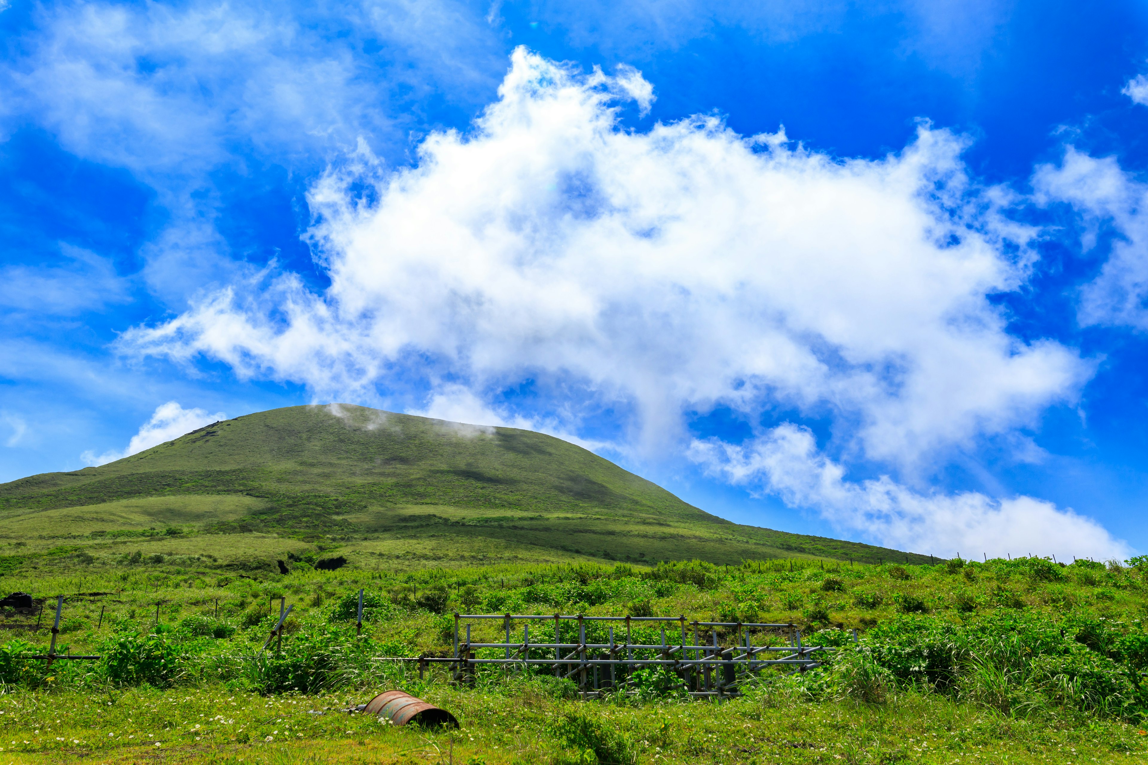 Pemandangan gunung hijau subur di bawah langit biru dengan awan putih