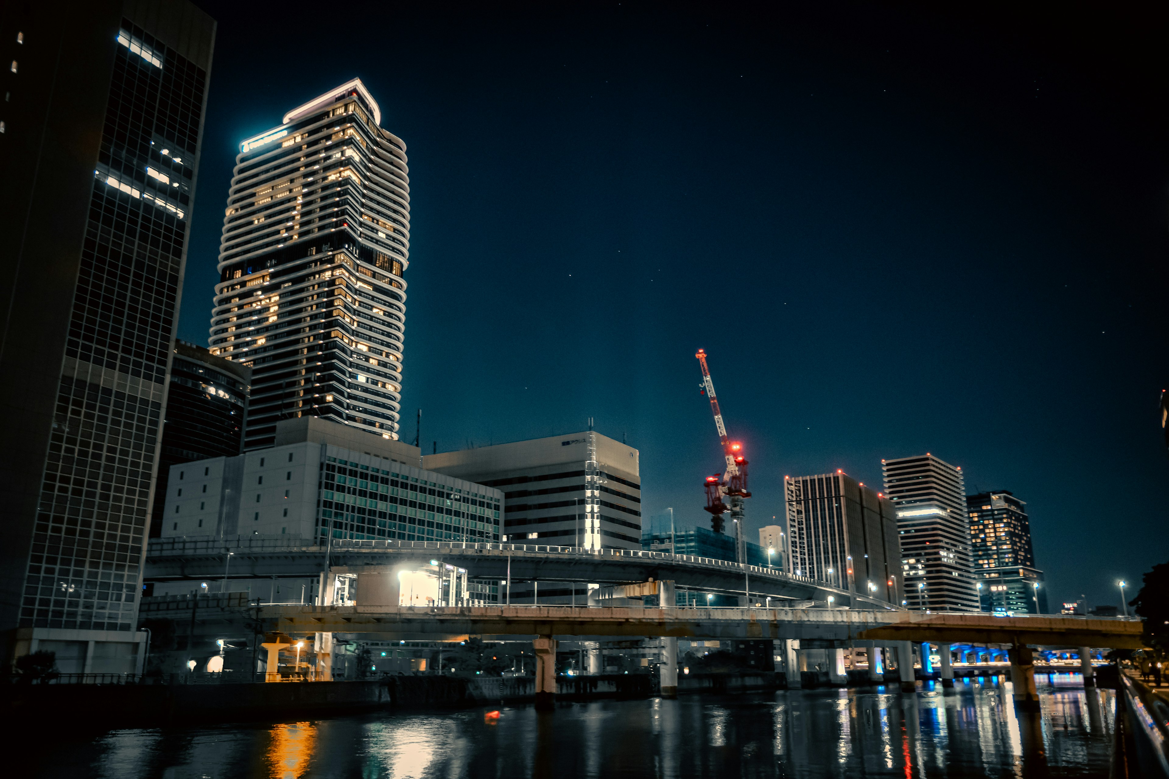 Cityscape at night featuring illuminated skyscrapers and river reflections