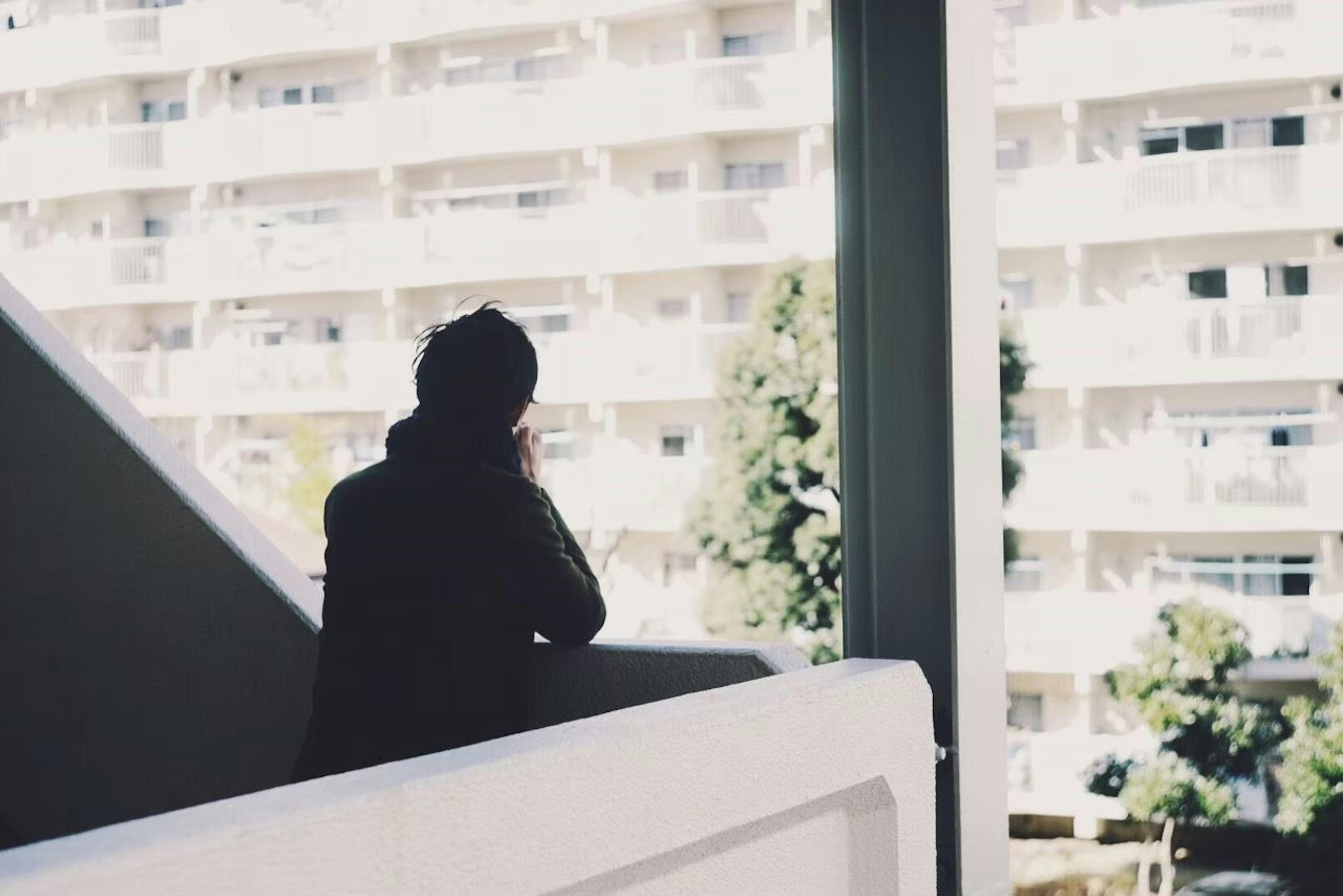 Silhouette of a person looking out the window at high-rise apartments