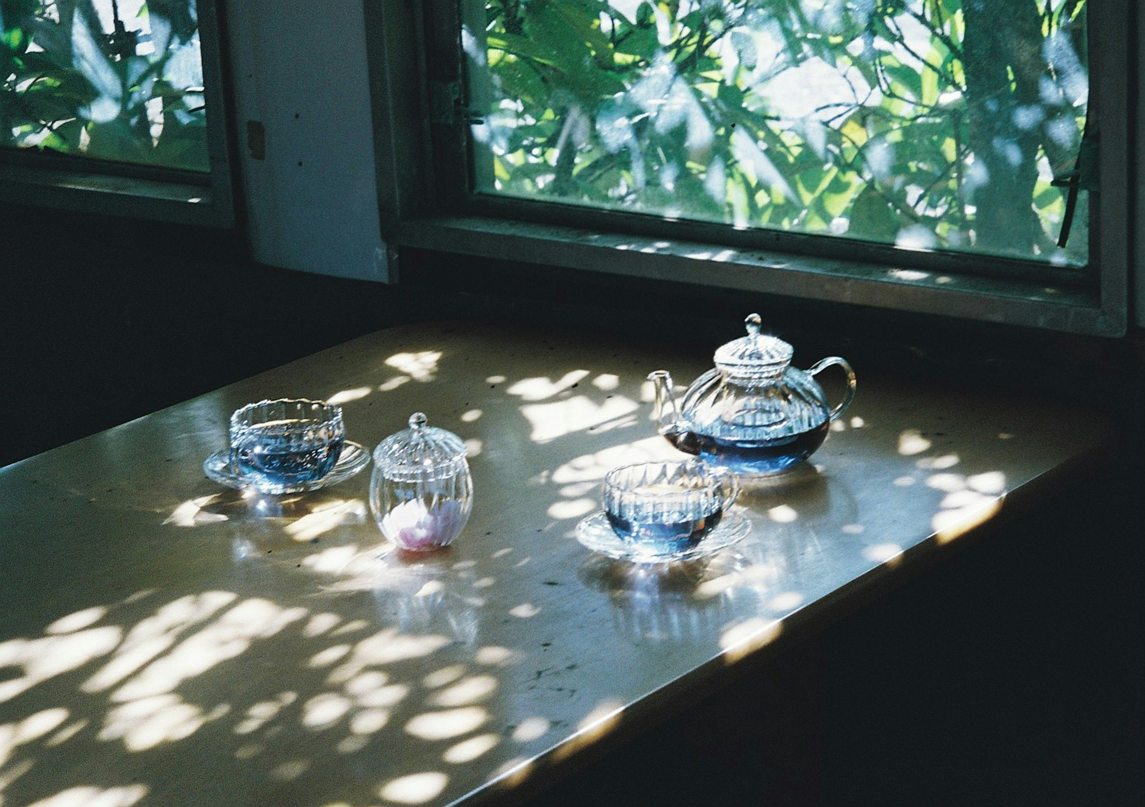 Transparent teapot and glass cups on a wooden table with soft shadows from window light