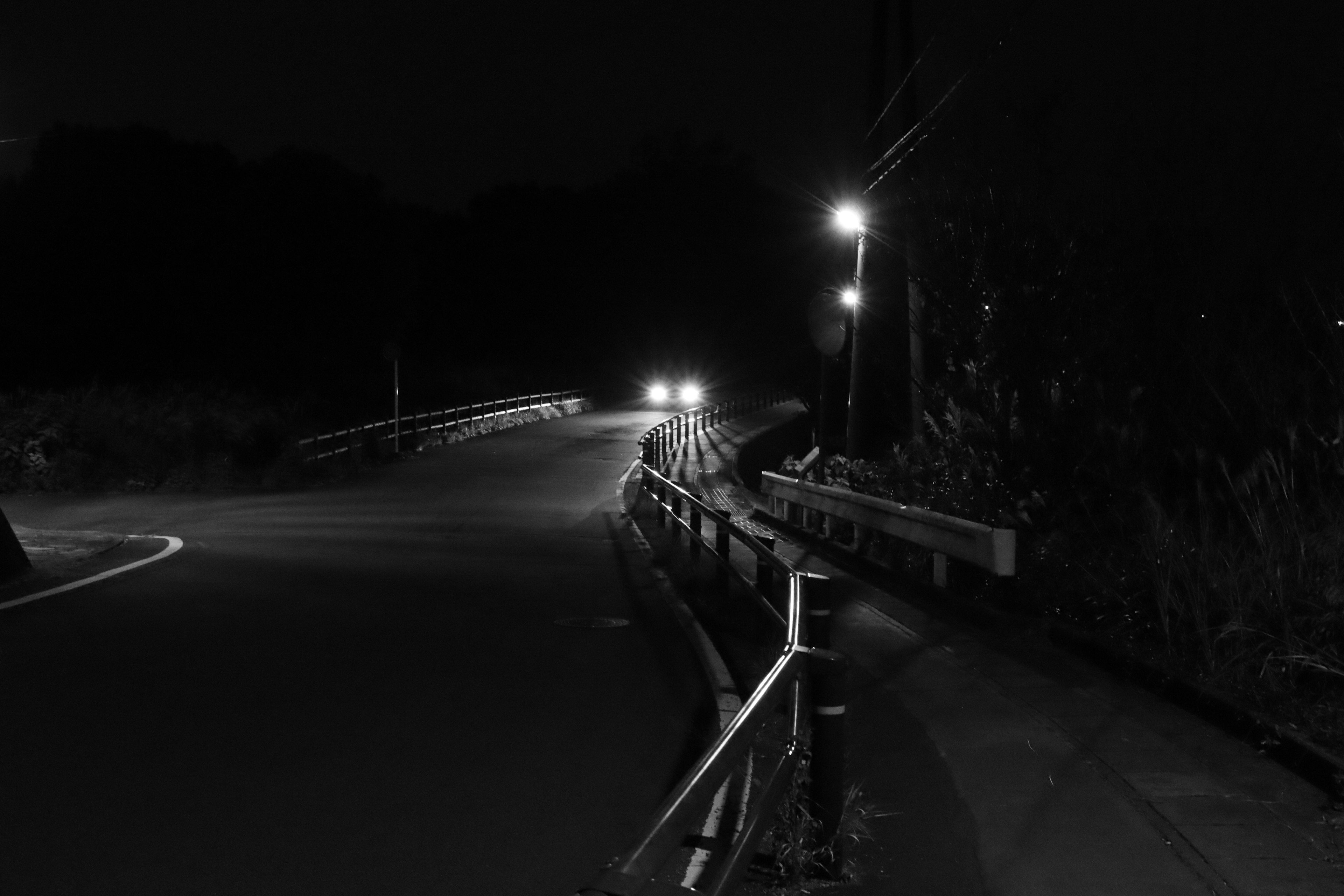 Dark road with a car's headlights illuminating a curve at night