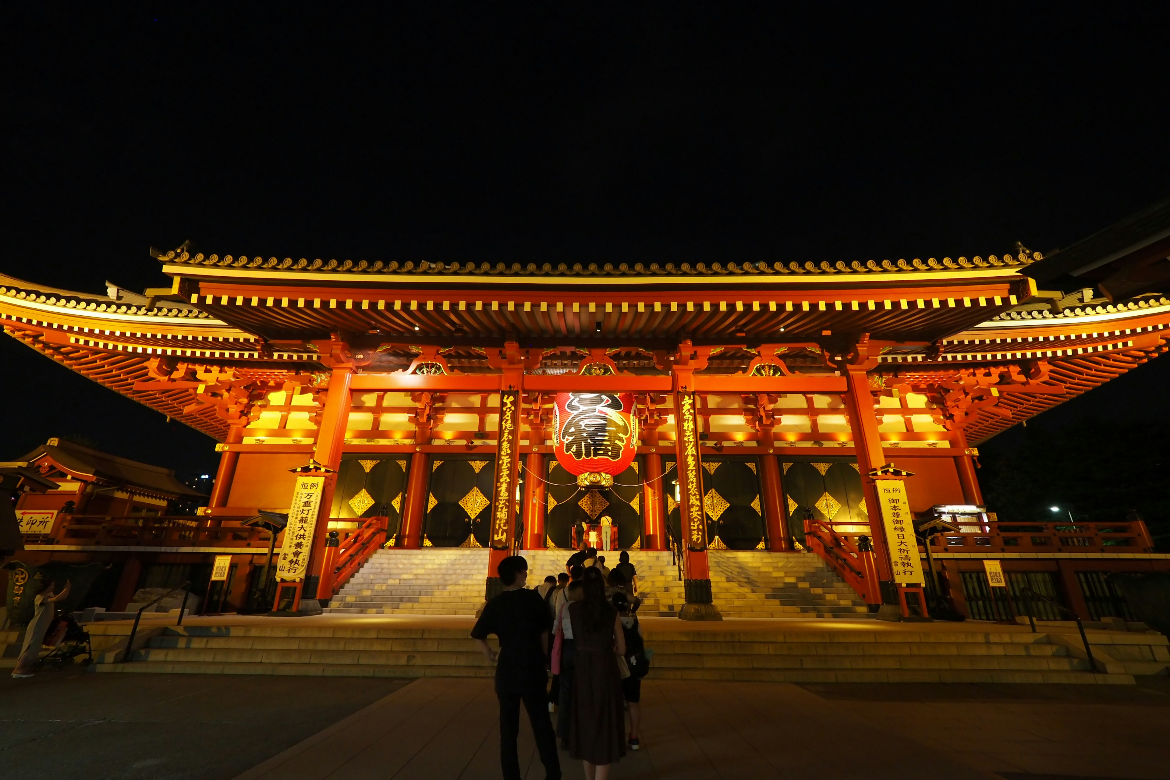 夜の明かりに照らされた赤い神社の門と人々の姿