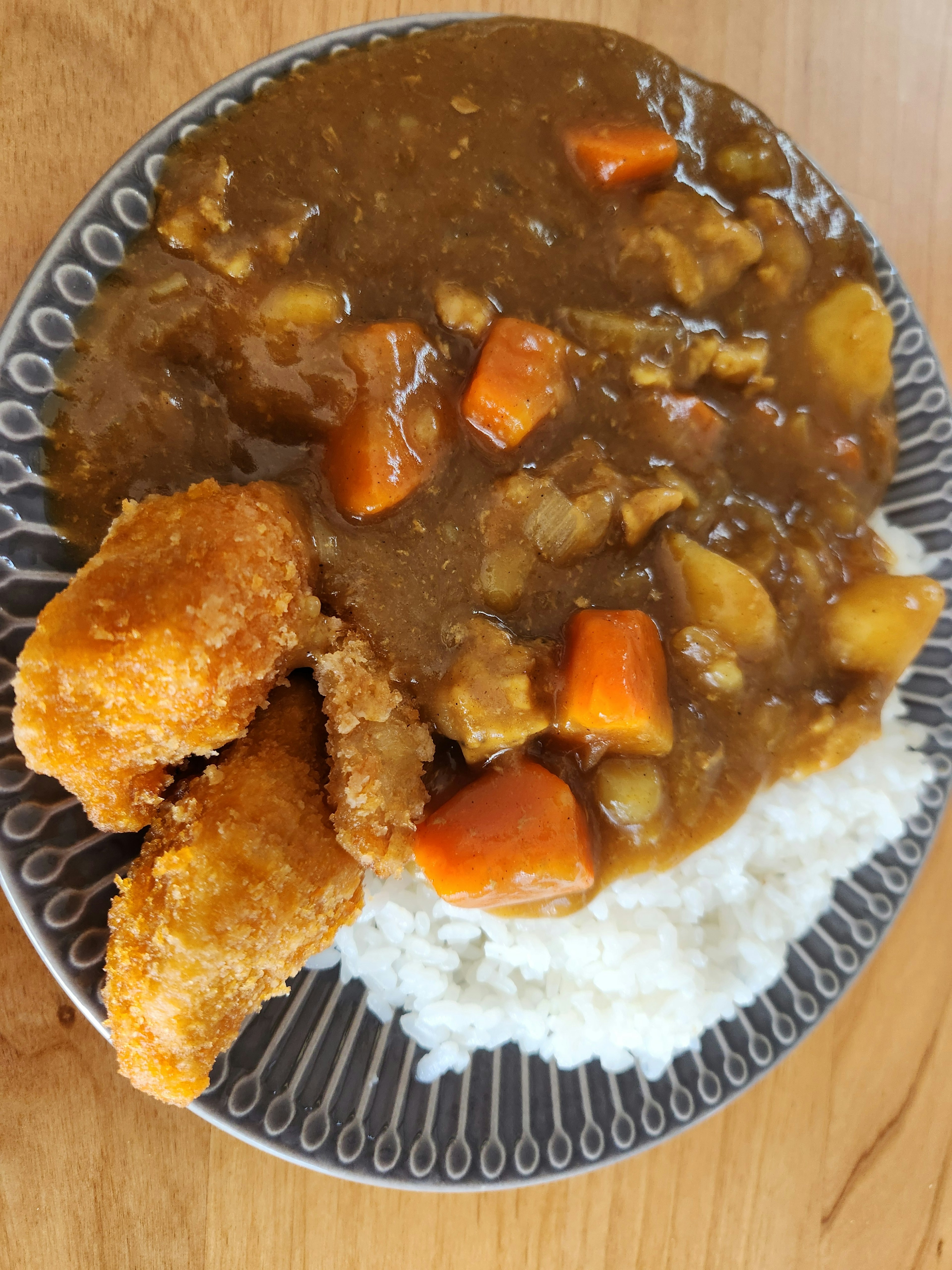 白ご飯の上にカレーと野菜がのった皿に、揚げ物が添えられている