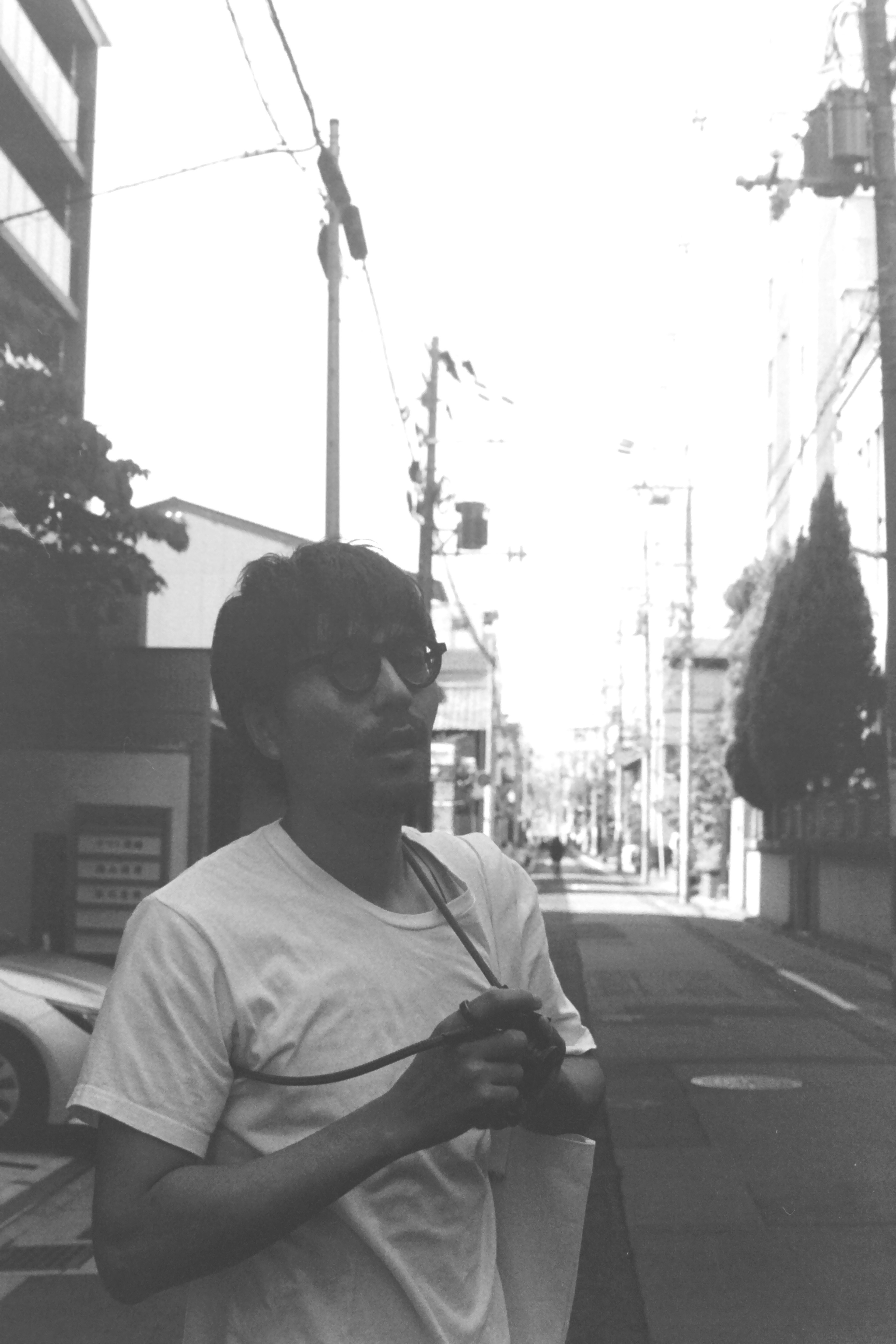 Young man standing at a street corner holding a camera with an urban backdrop in black and white