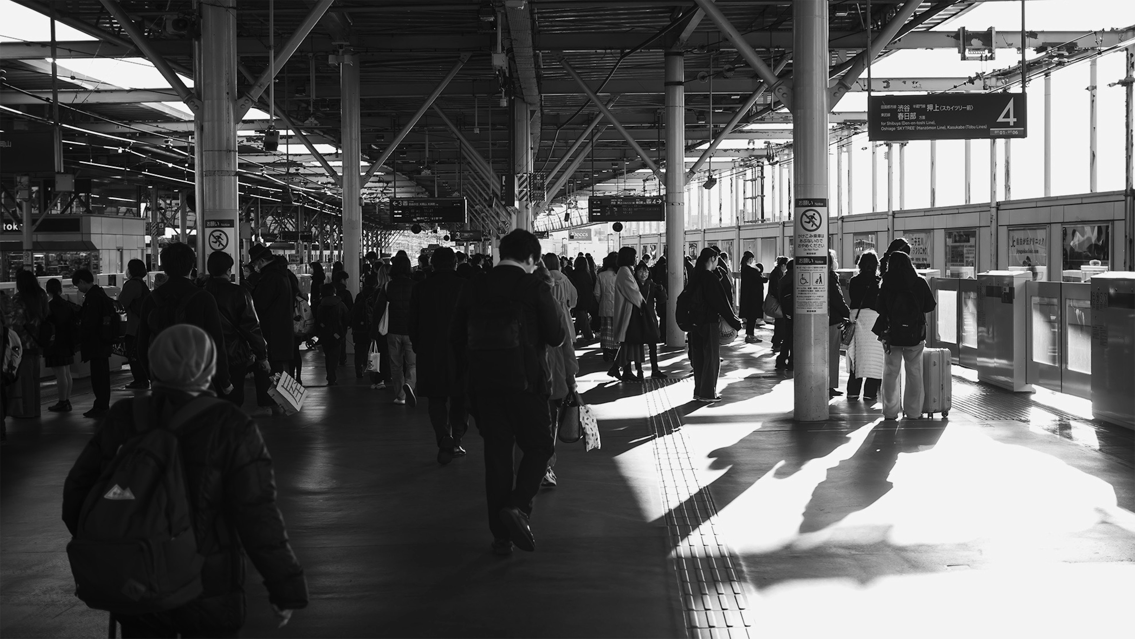 Black and white scene of a busy train station with many people walking