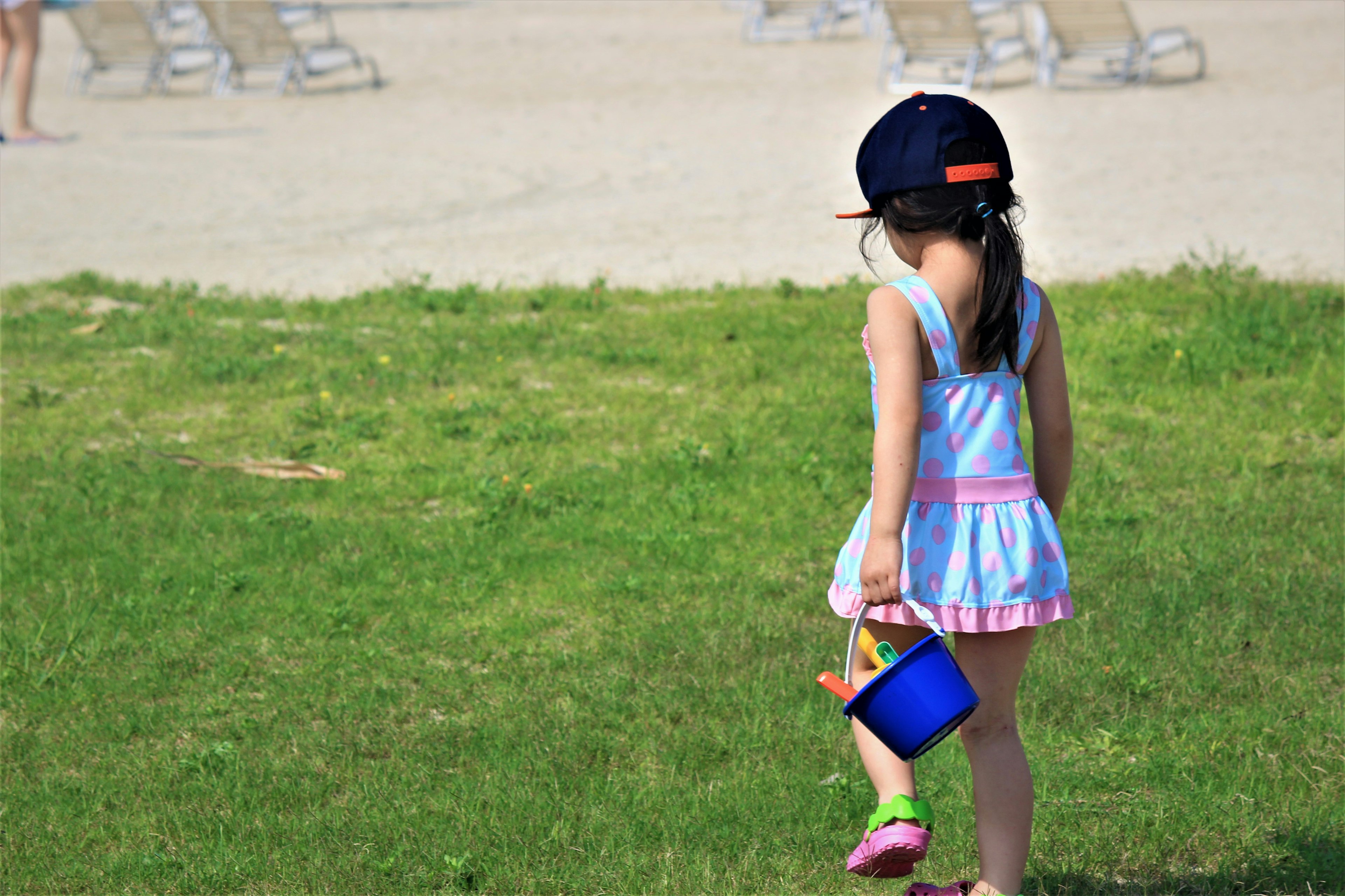 A girl walking on grass holding a blue bucket