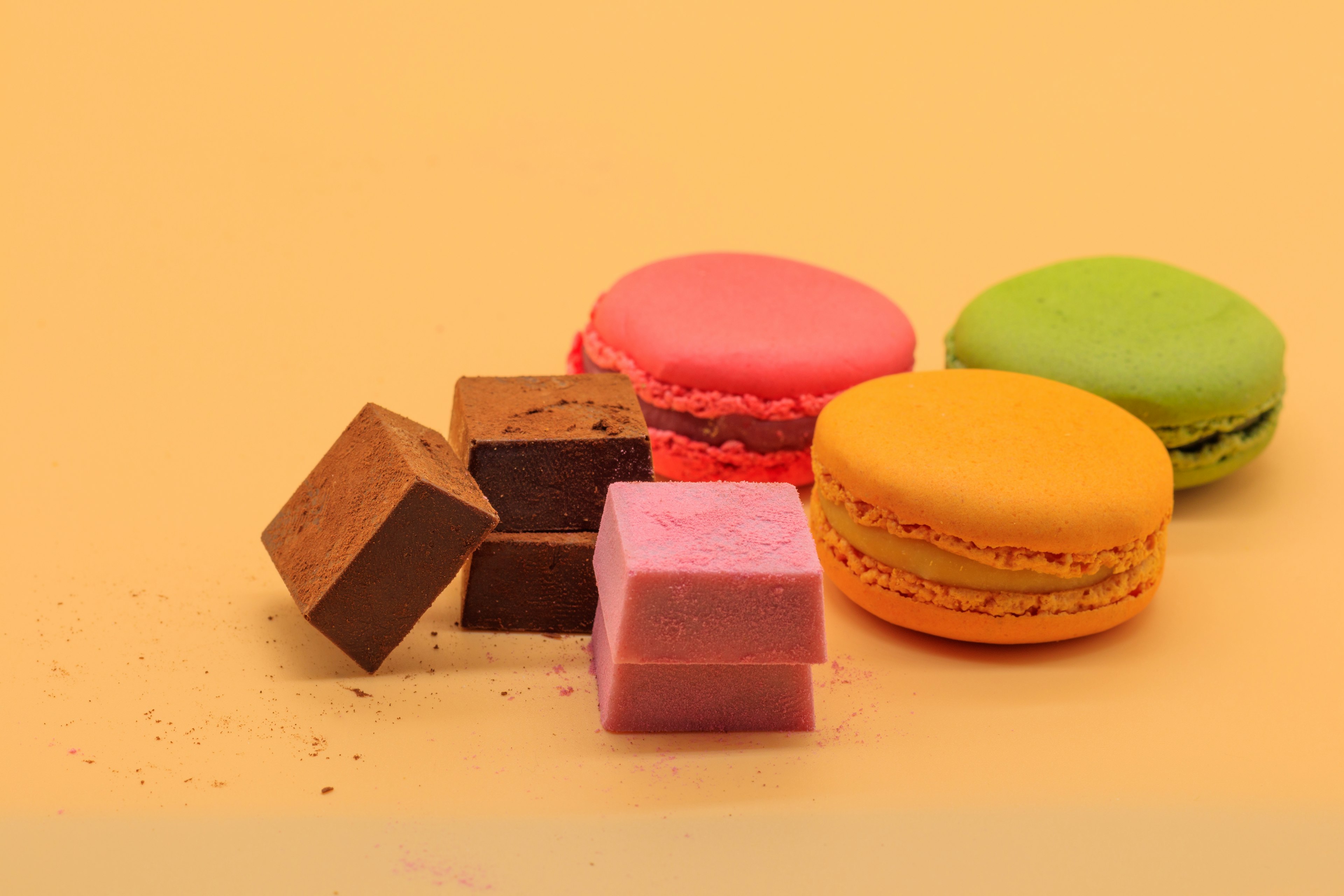 Macarons colorés et cubes de chocolat disposés sur un fond jaune