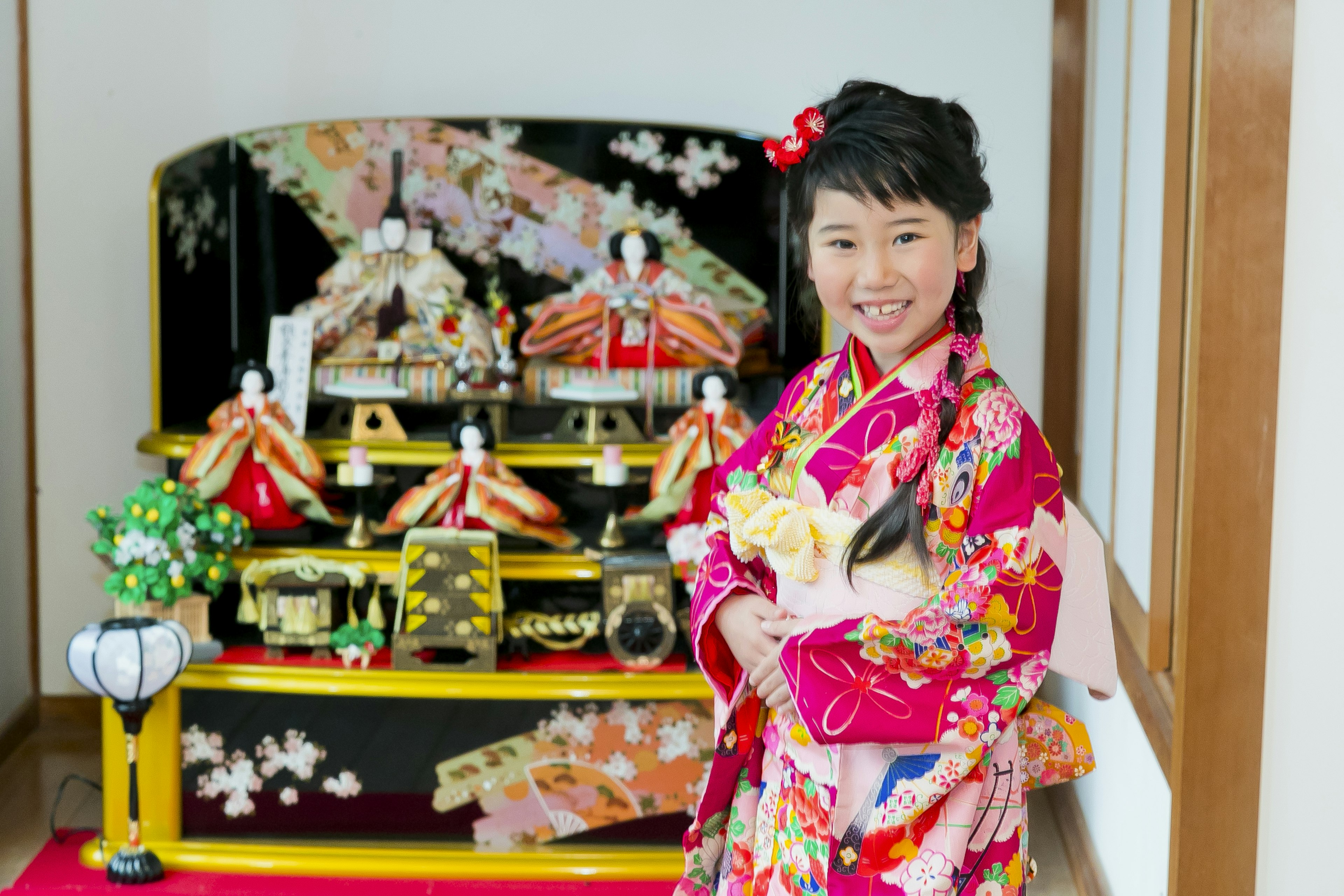 Una niña con un kimono colorido sonriendo con una exhibición tradicional de Hina Matsuri de fondo