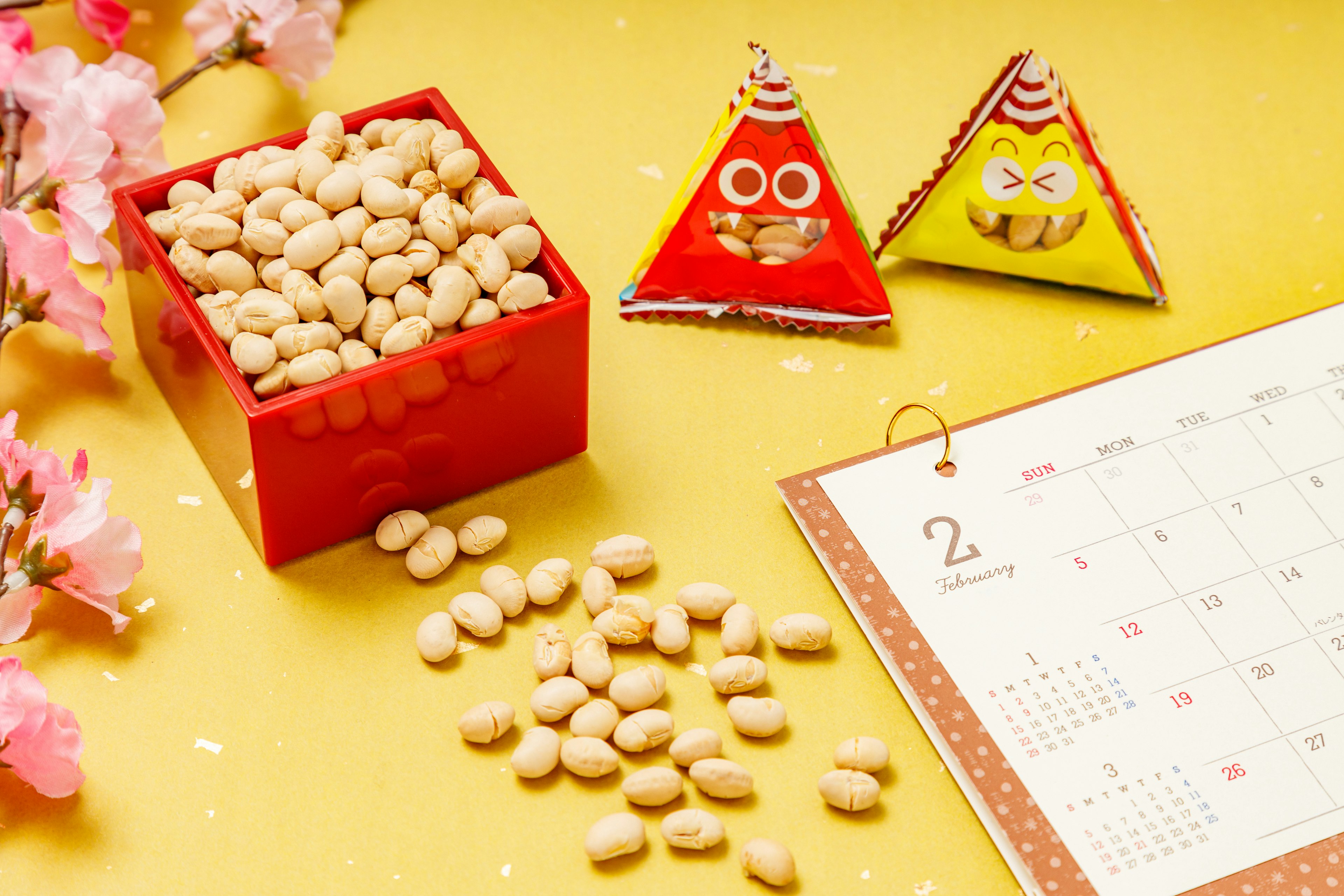 A red box filled with beans next to triangular candies with faces on a yellow background