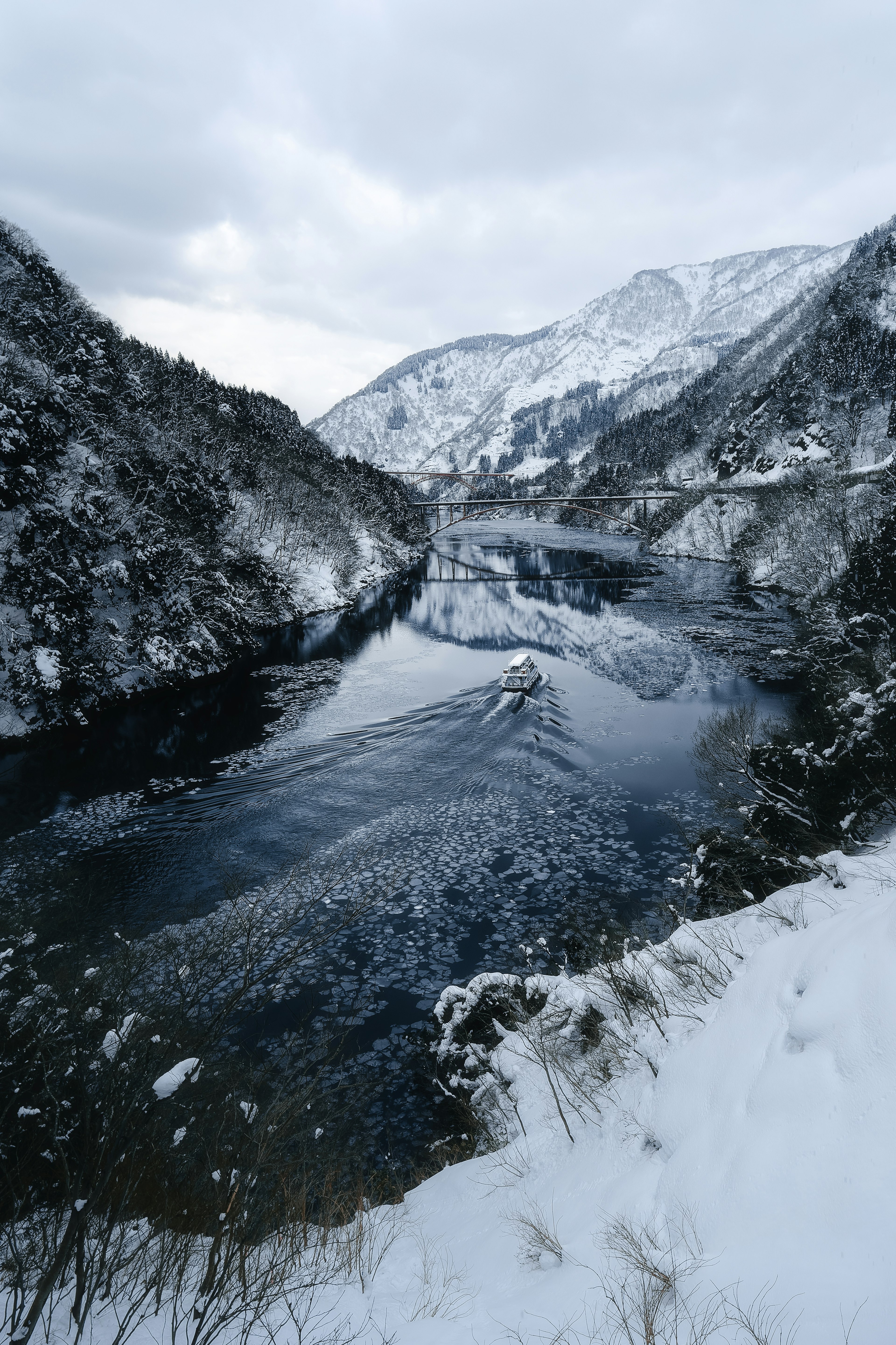 雪に覆われた山々の間を流れる静かな川の風景