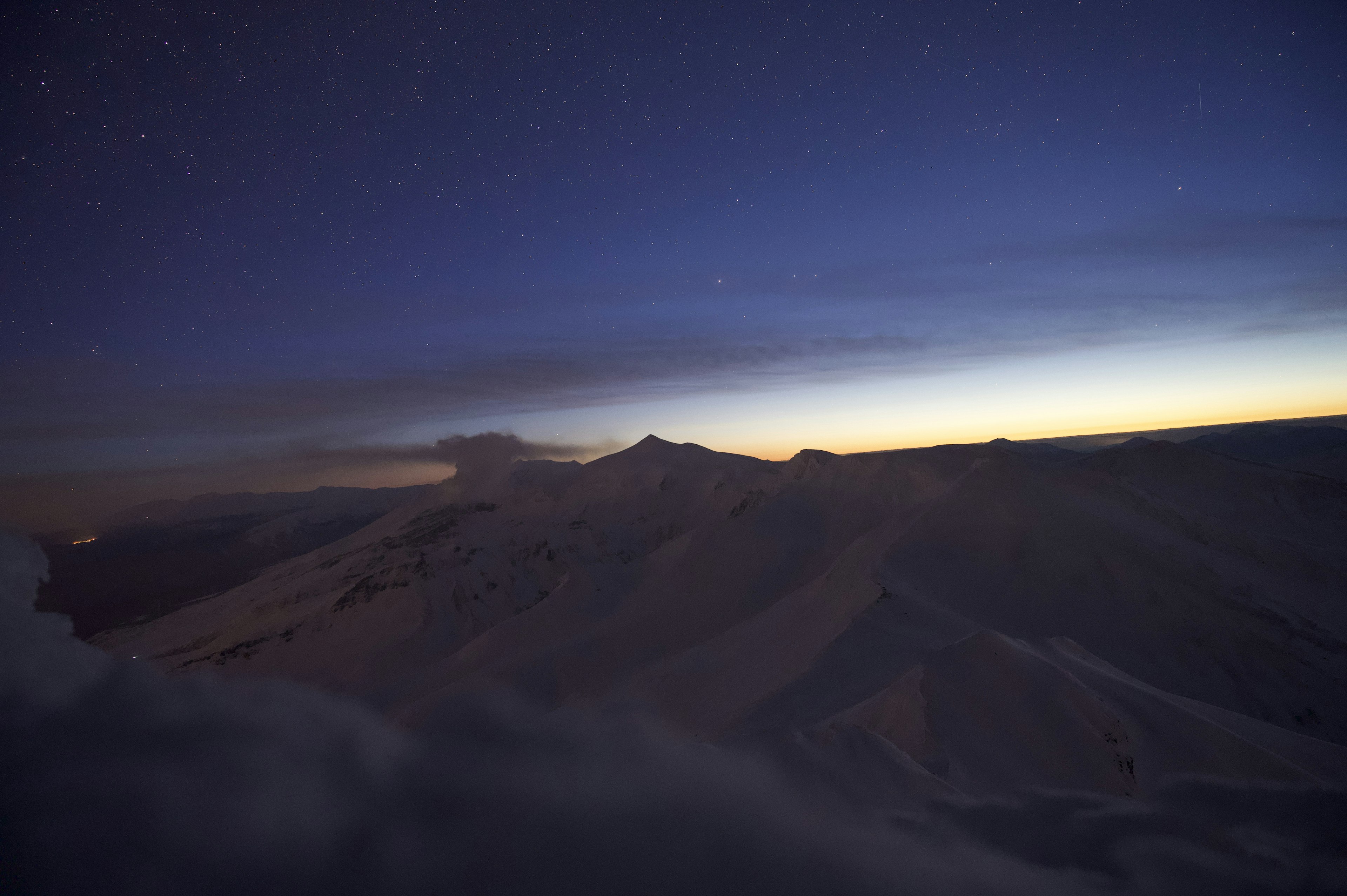 Silueta de montañas bajo un cielo estrellado con luz del amanecer