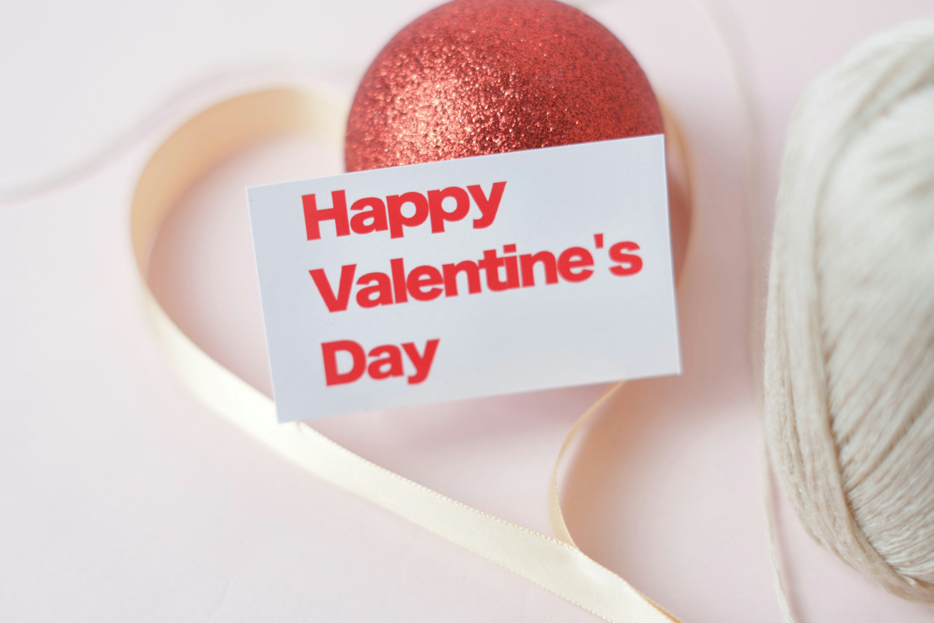 A festive card with a Happy Valentine's Day message alongside a red glittery ornament on a heart-shaped ribbon