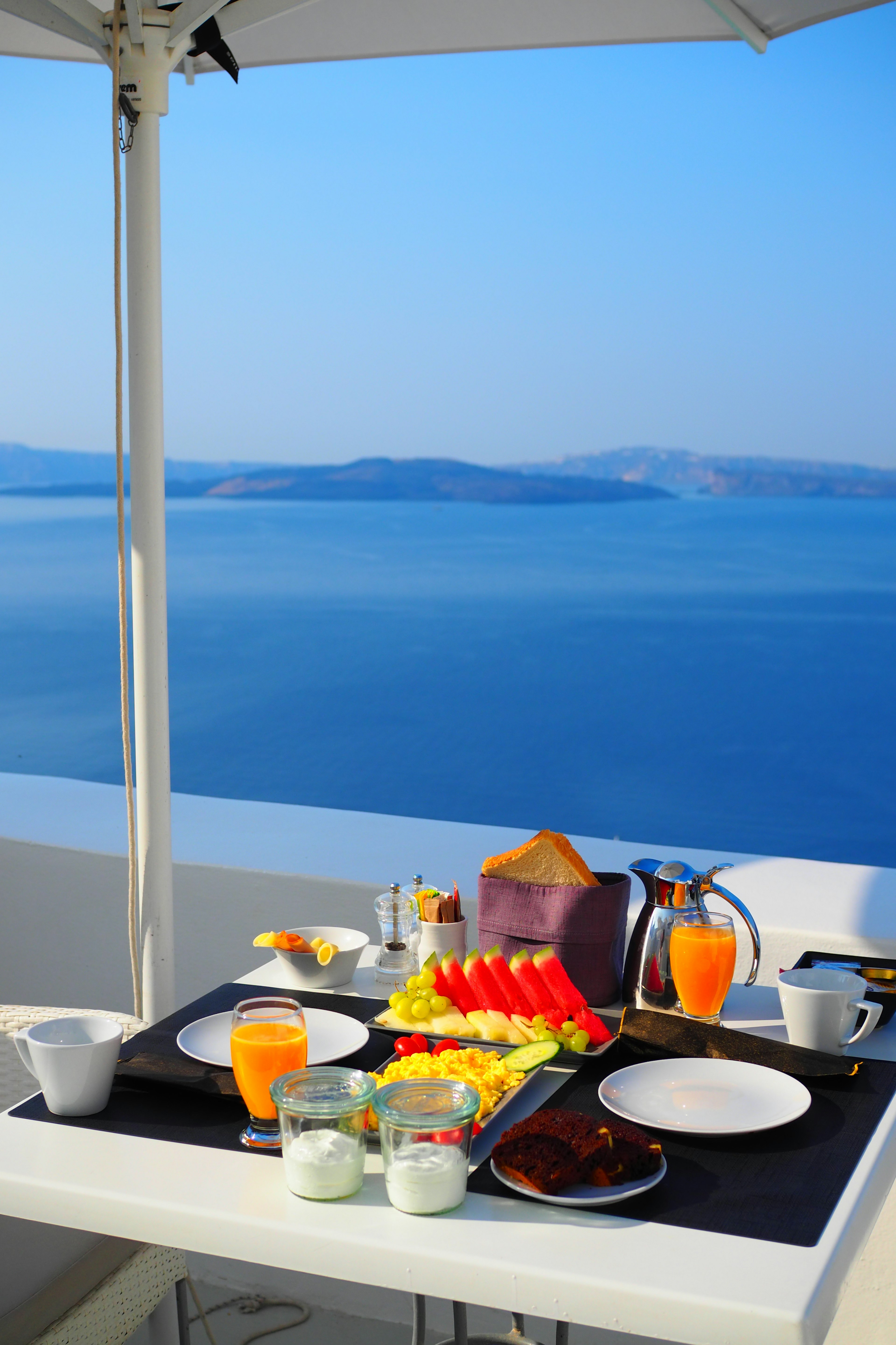 Frühstücksszene auf einer Terrasse mit Blick auf das Meer verschiedene Früchte und Getränke auf dem Tisch