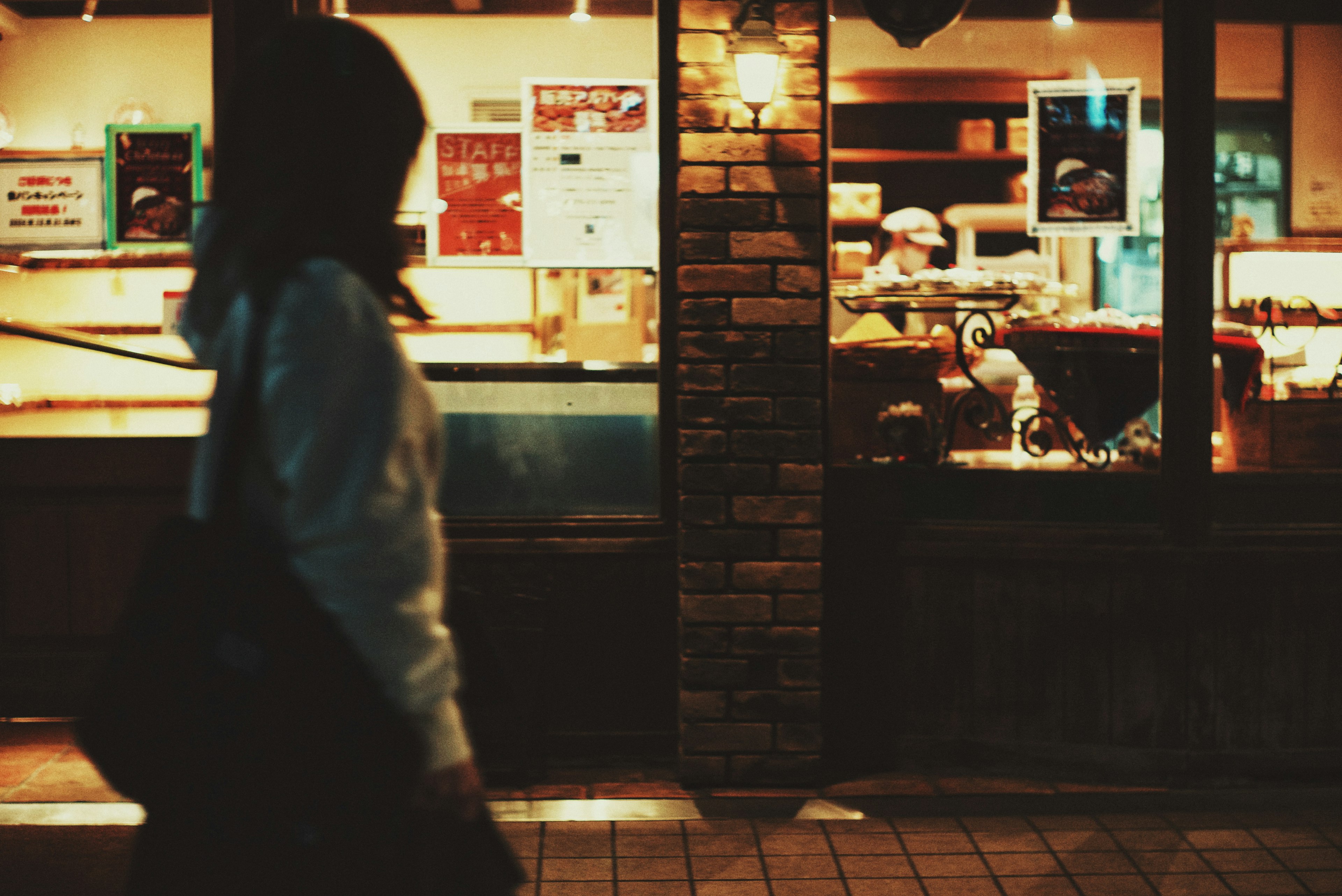 Woman walking on a dark street beside a brightly lit café window