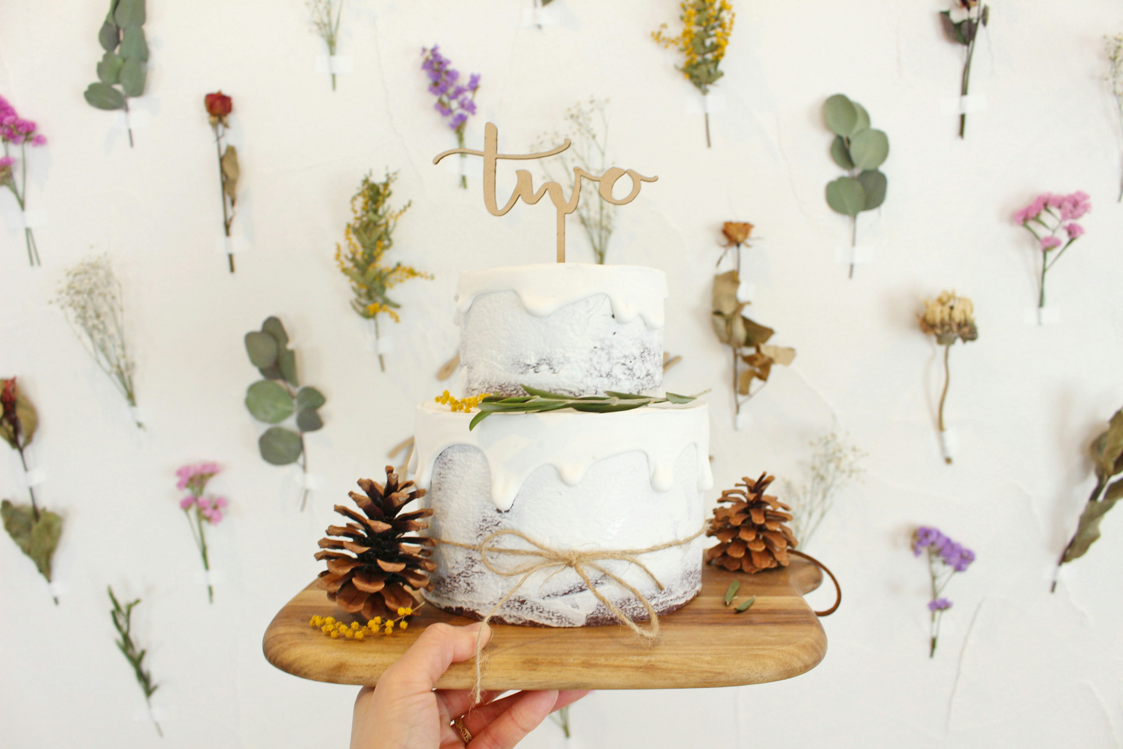 Gâteau blanc à deux niveaux décoré de fleurs séchées et de pommes de pin