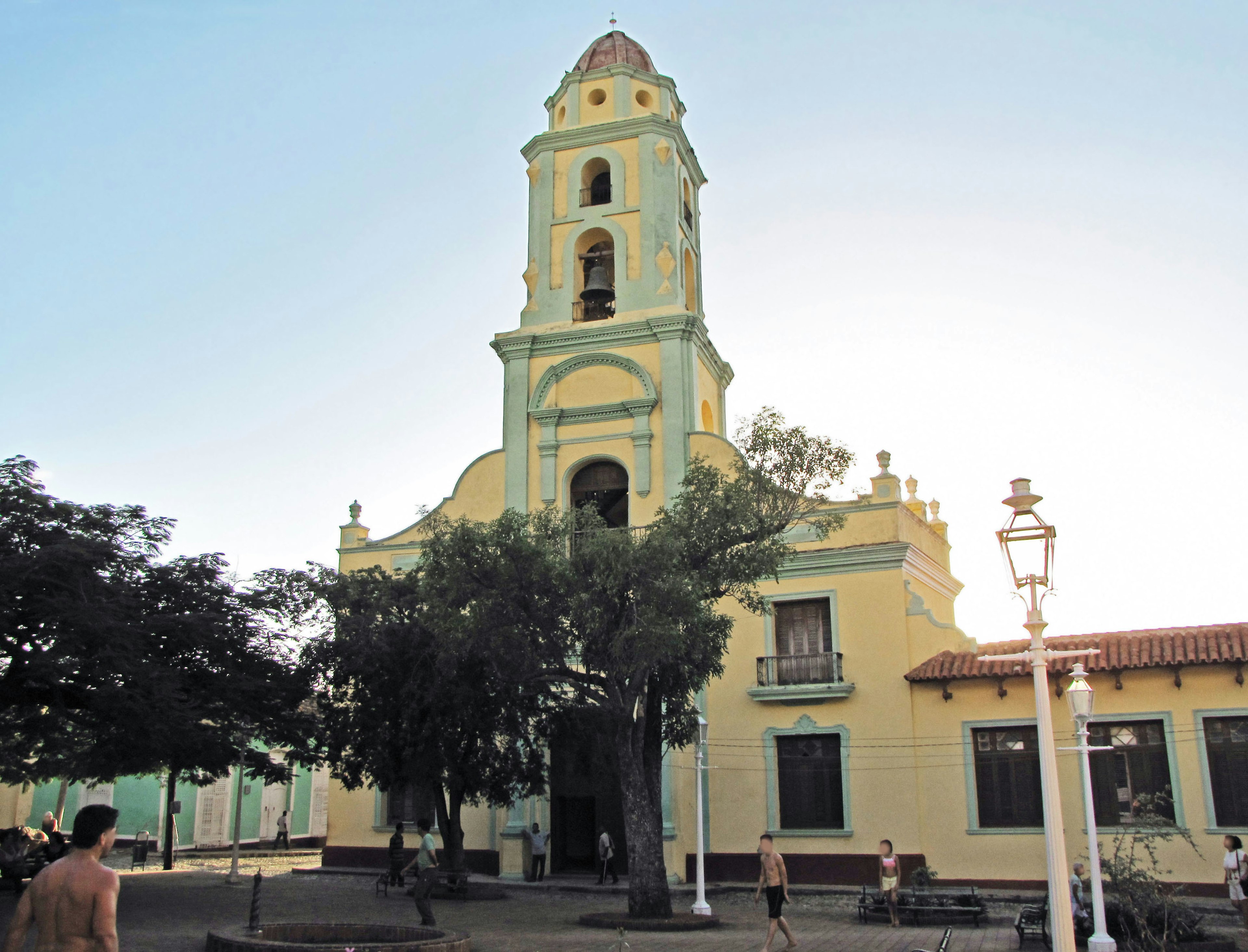 Fachada de una iglesia con paredes azules y amarillas Árboles y personas a la luz del sol