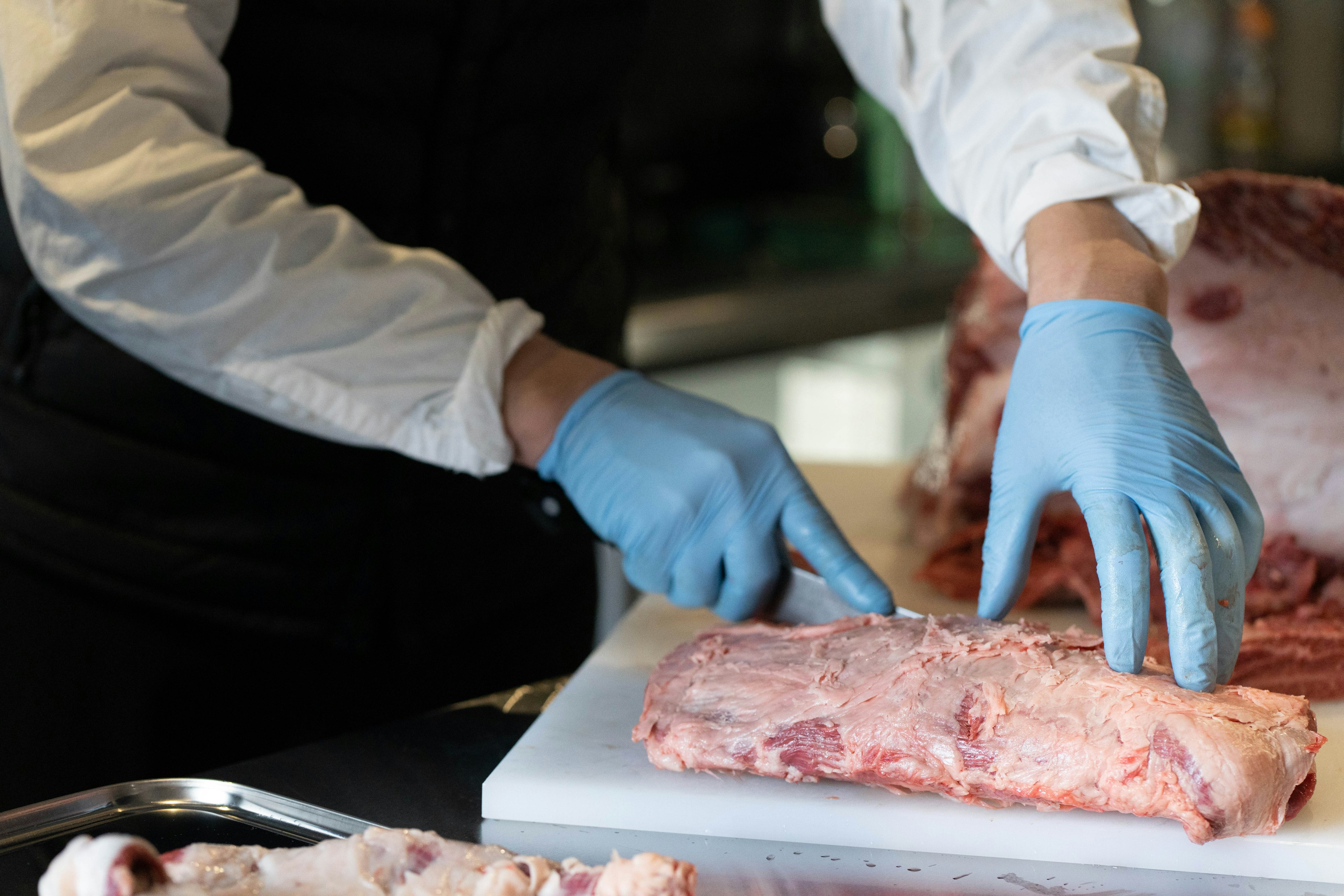 Mani di chef che tagliano carne su un tagliere bianco