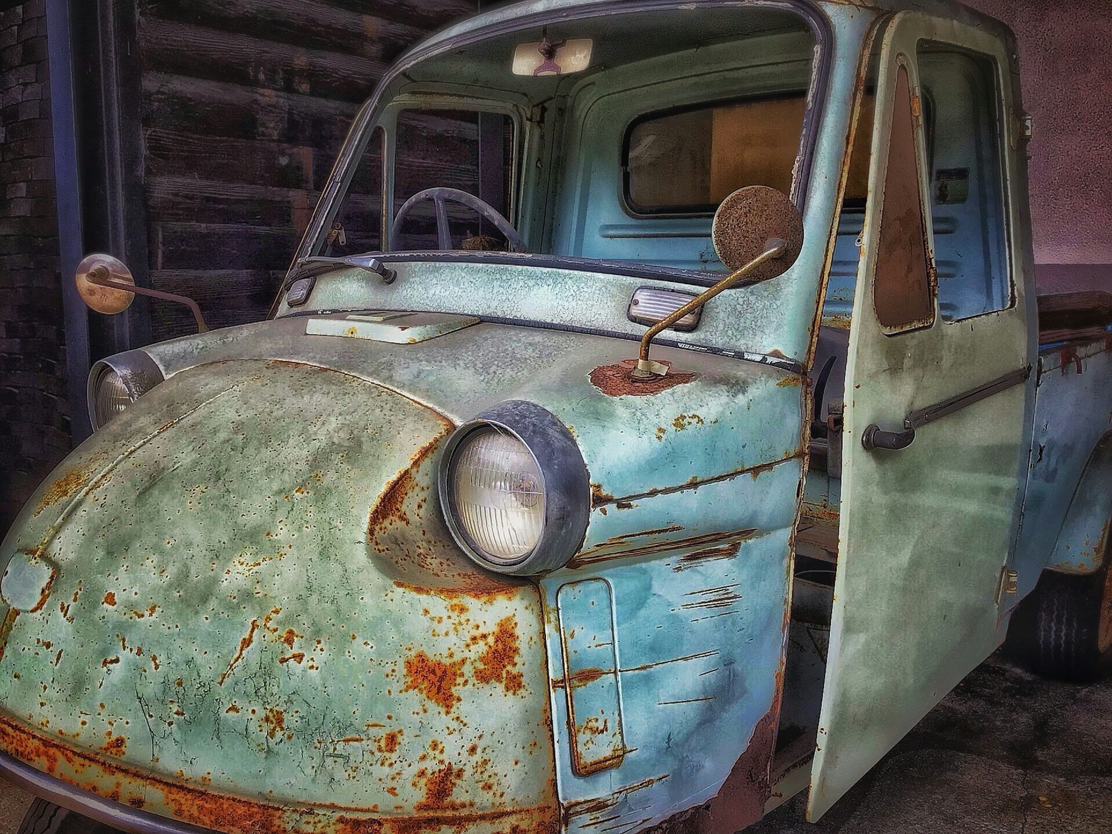 Image of an old blue truck with a unique shape featuring rust and a side view of the driver's seat