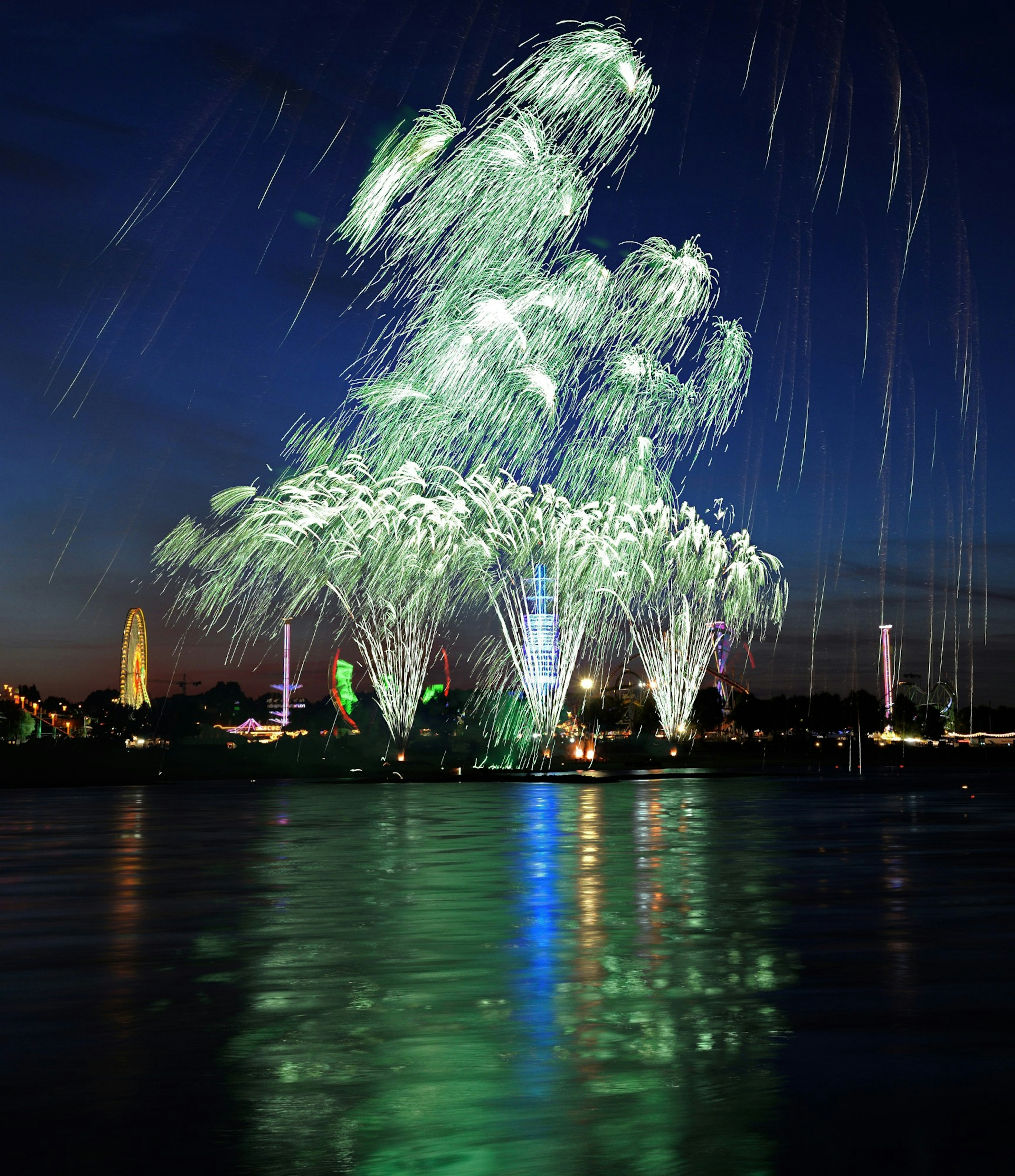 Green fireworks display lighting up the night sky with reflections on the water