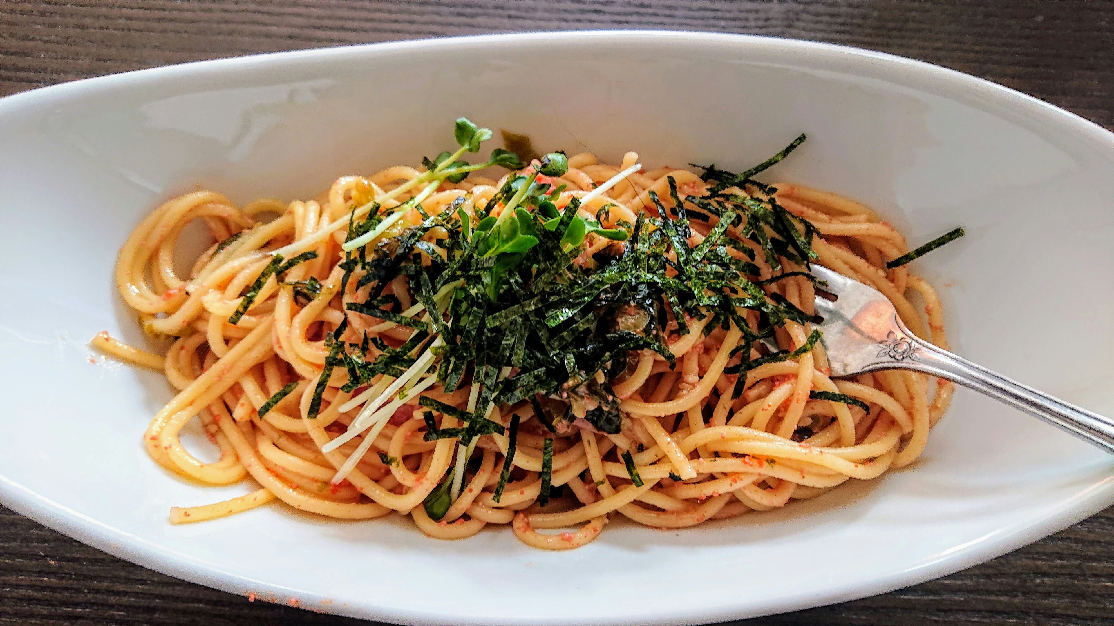 Pasta served on a white plate topped with seaweed and chopped green onions