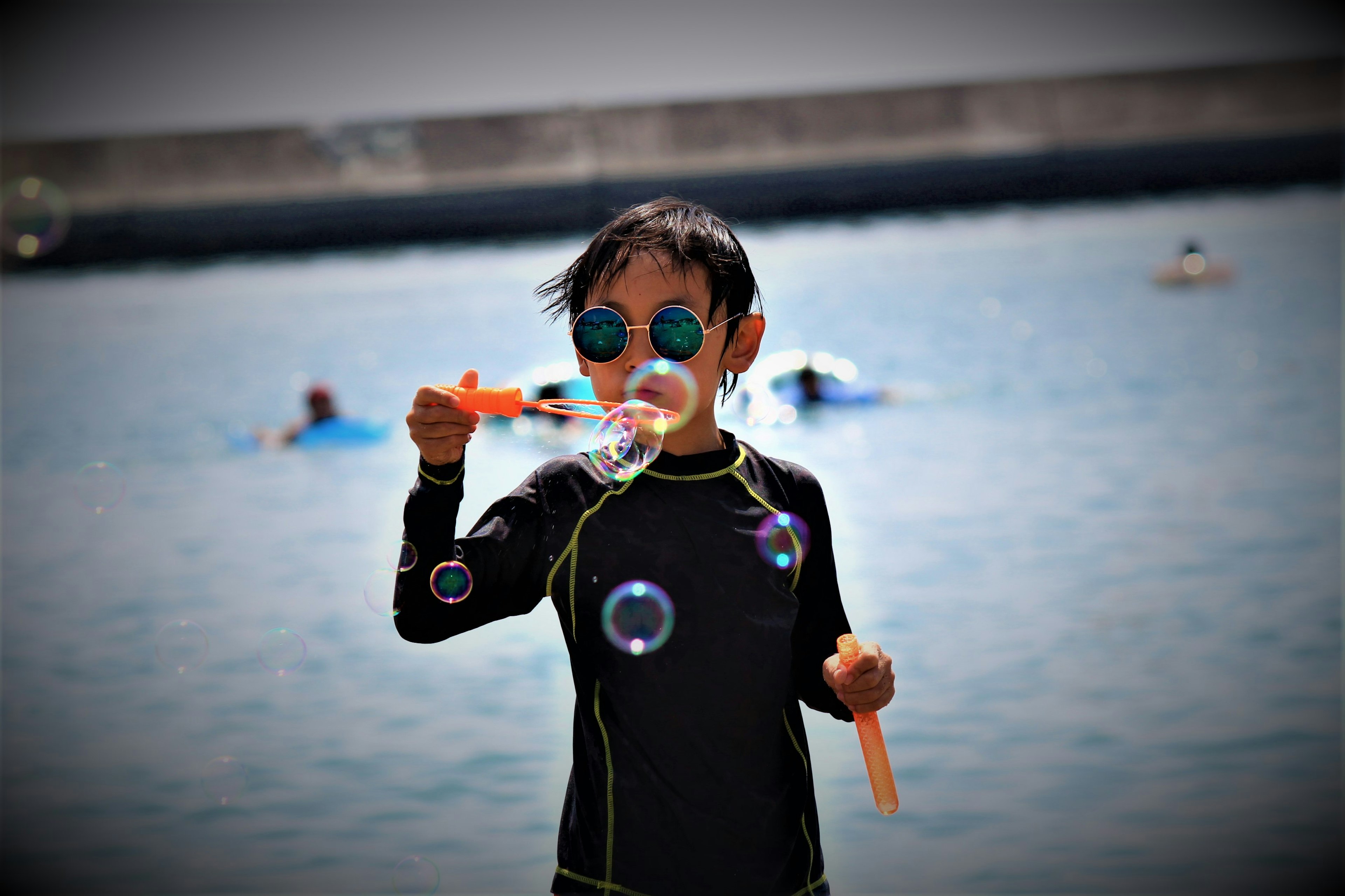 Bambino che soffia bolle in spiaggia indossando una muta nera e occhiali blu