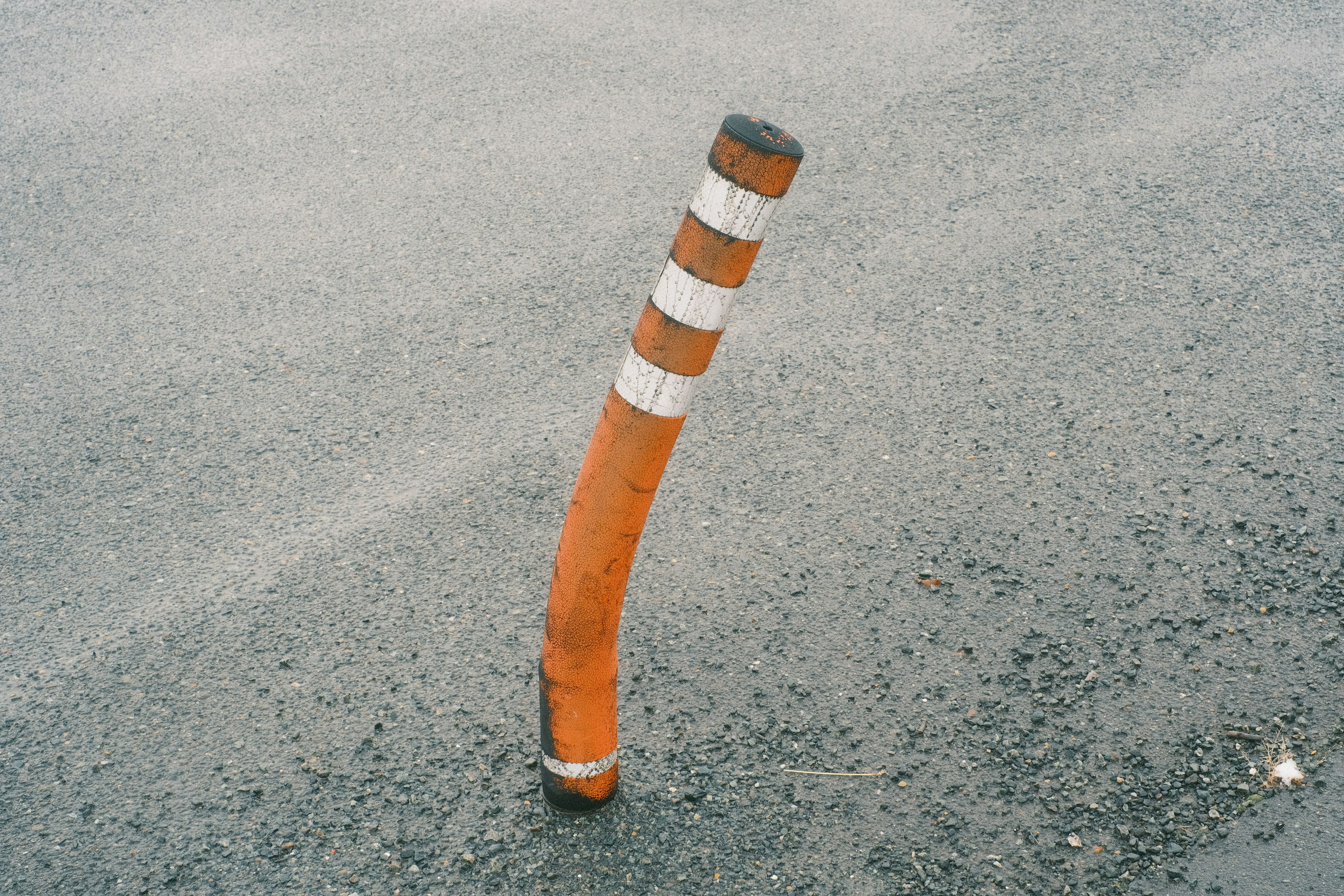 Poste naranja doblado con rayas blancas sobre asfalto