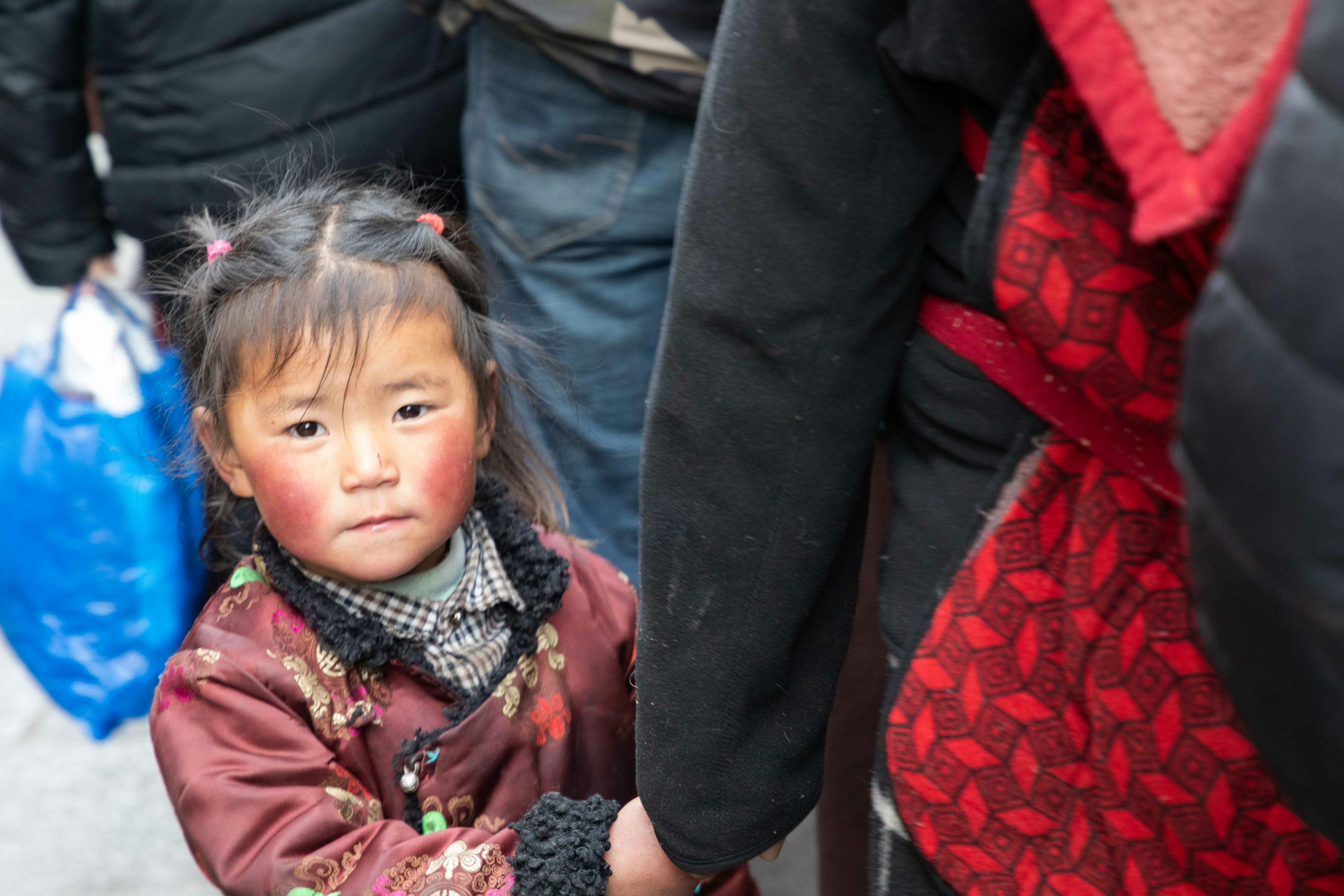 A young girl holding an adult's hand with rosy cheeks wearing traditional clothing