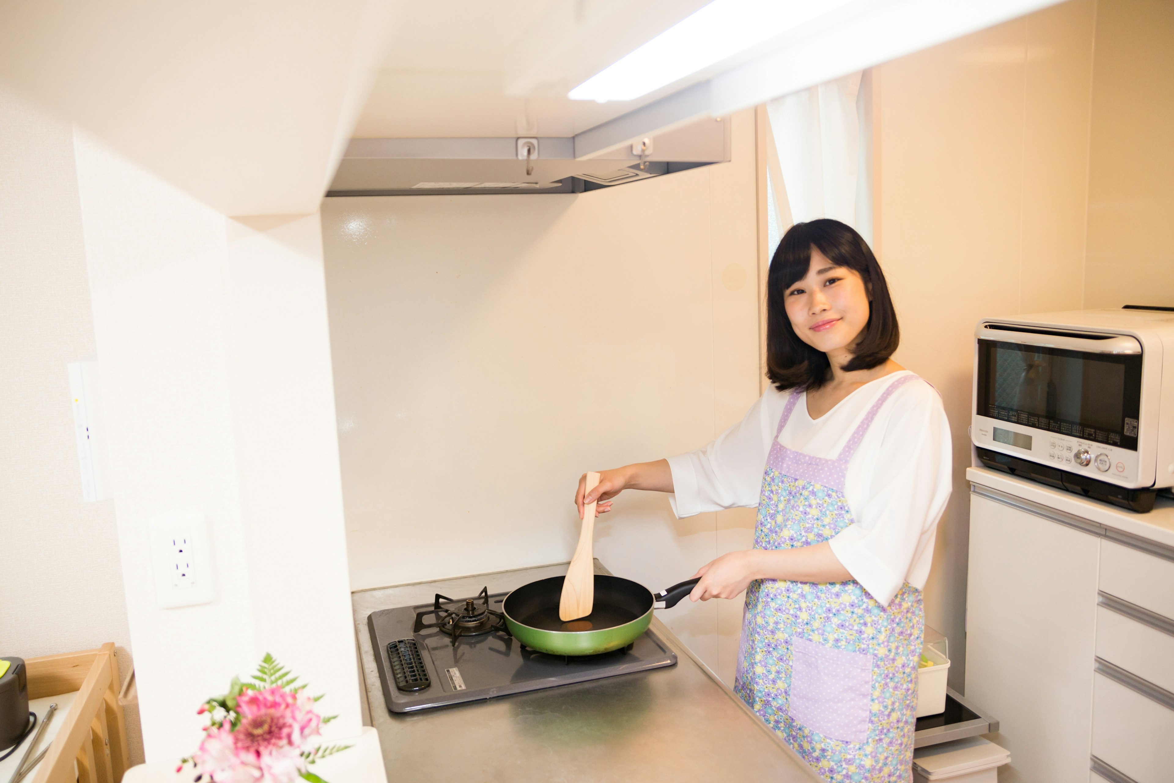 Wanita memasak di dapur tersenyum sambil memegang wajan