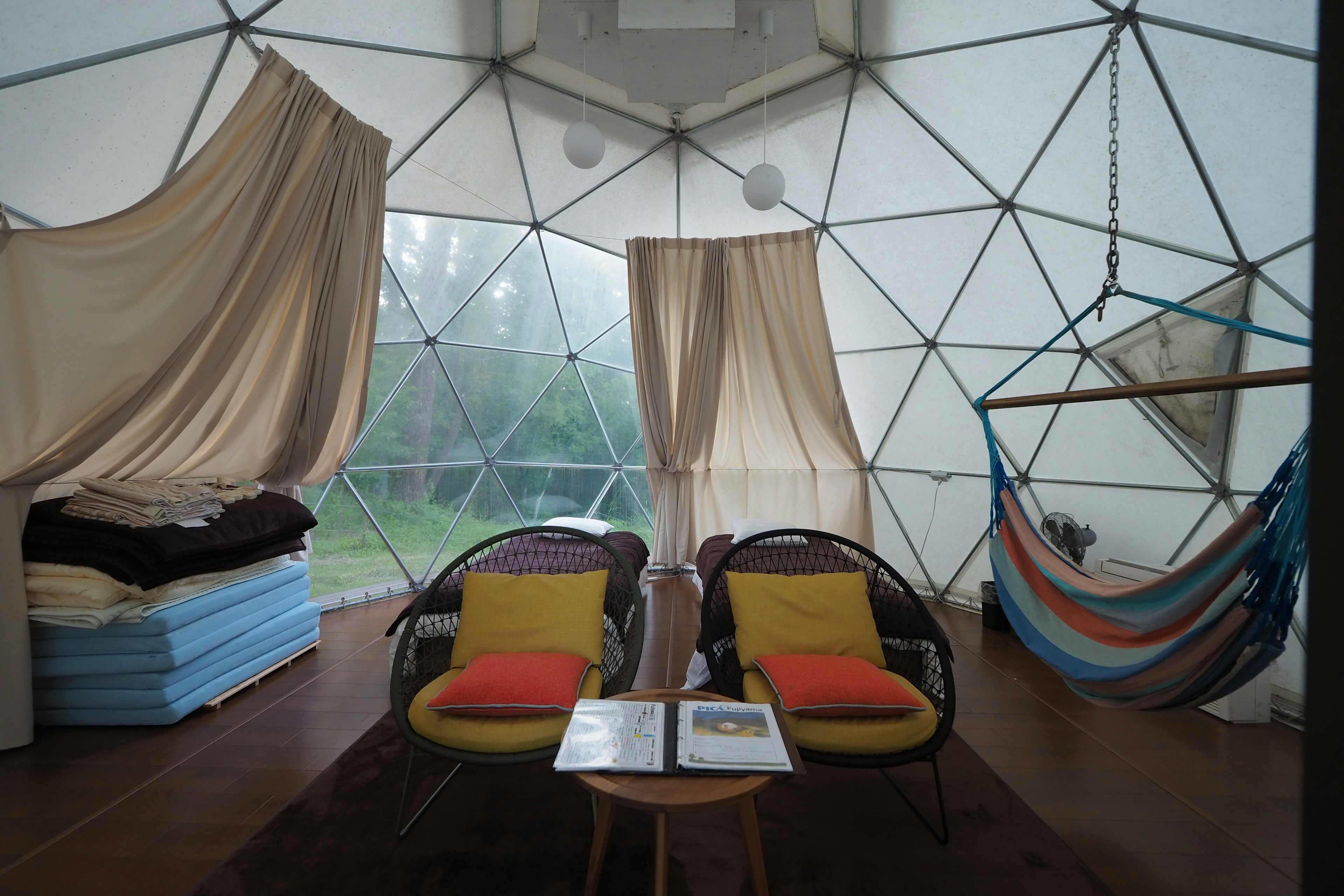 Interior de un alojamiento en cúpula geodésica con sillas coloridas y una hamaca