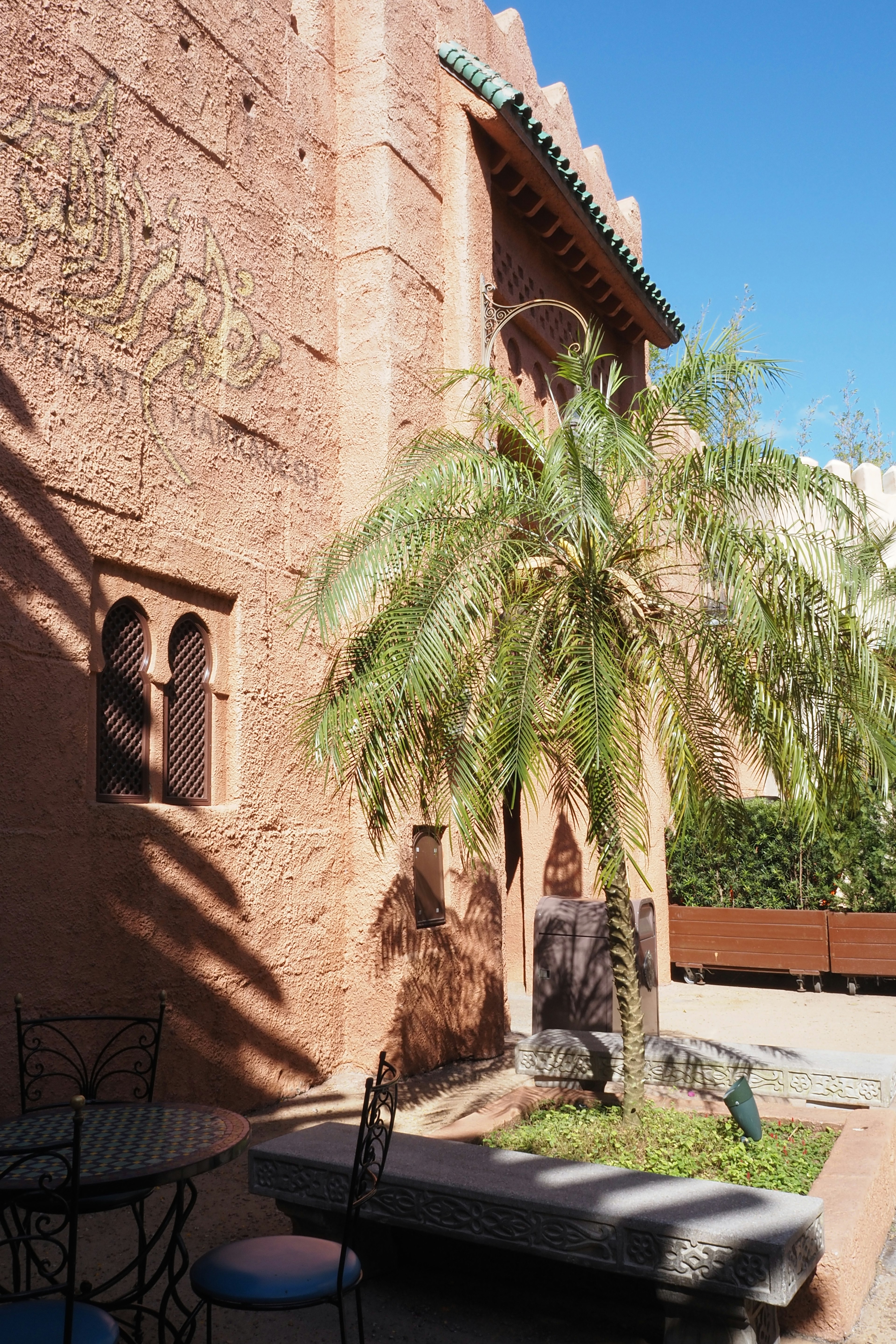 Parte de un edificio con paredes rojo oscuro y ventanas que presentan una palmera