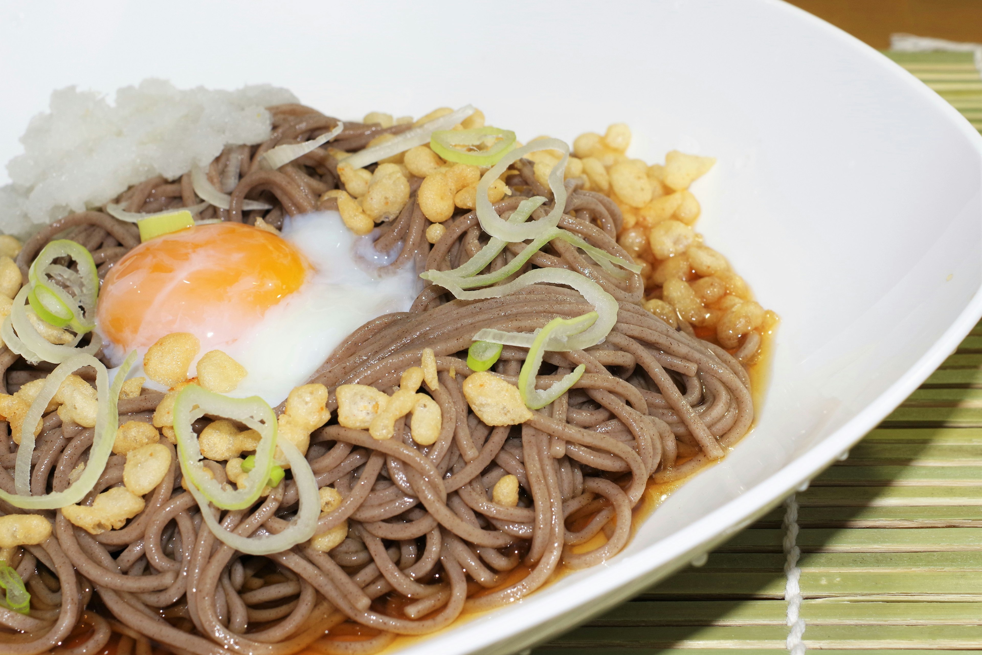 A bowl of soba noodles topped with a poached egg green onions and crushed nuts