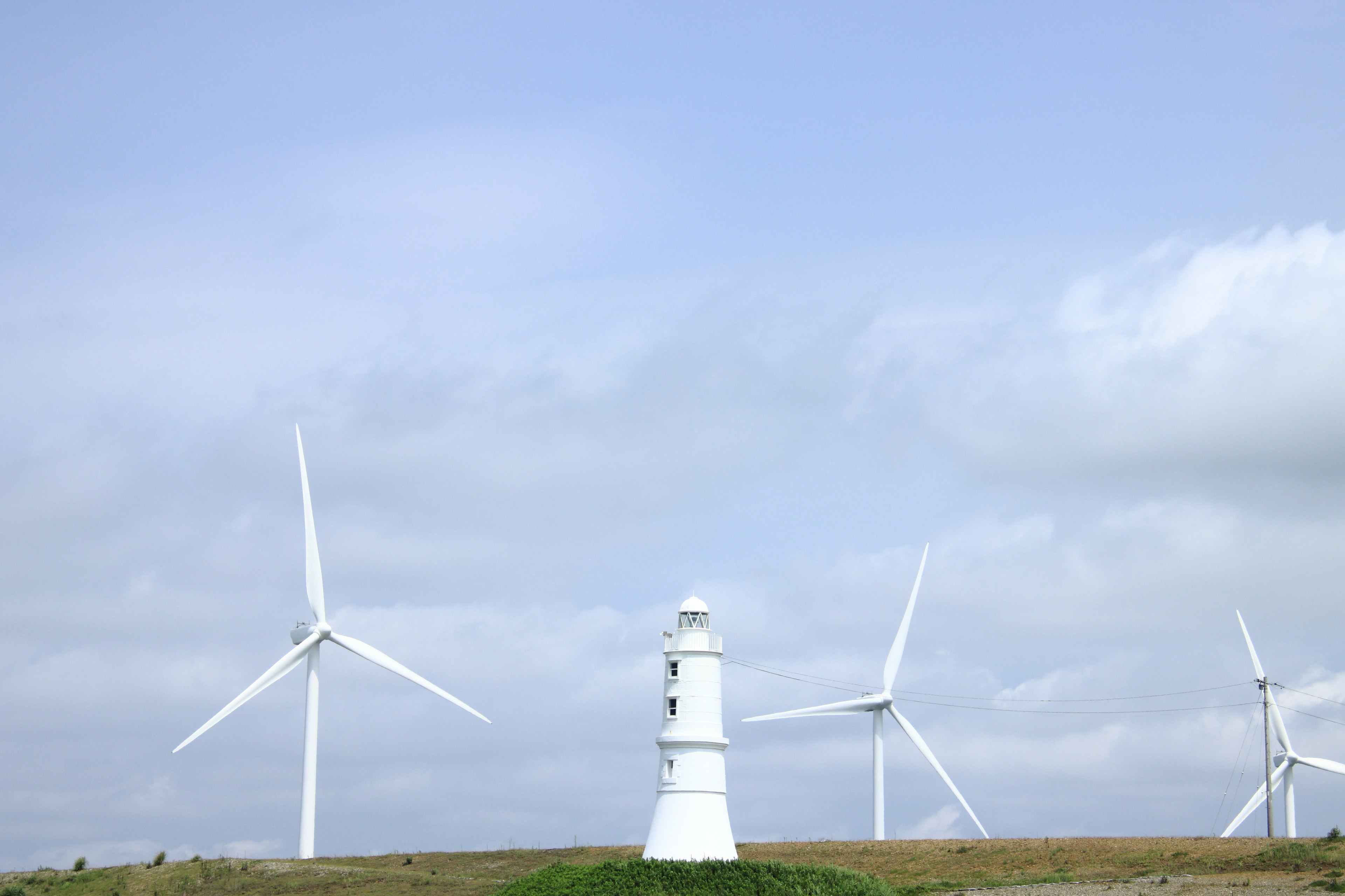 Landschaft mit Windkraftanlagen und einem weißen Leuchtturm