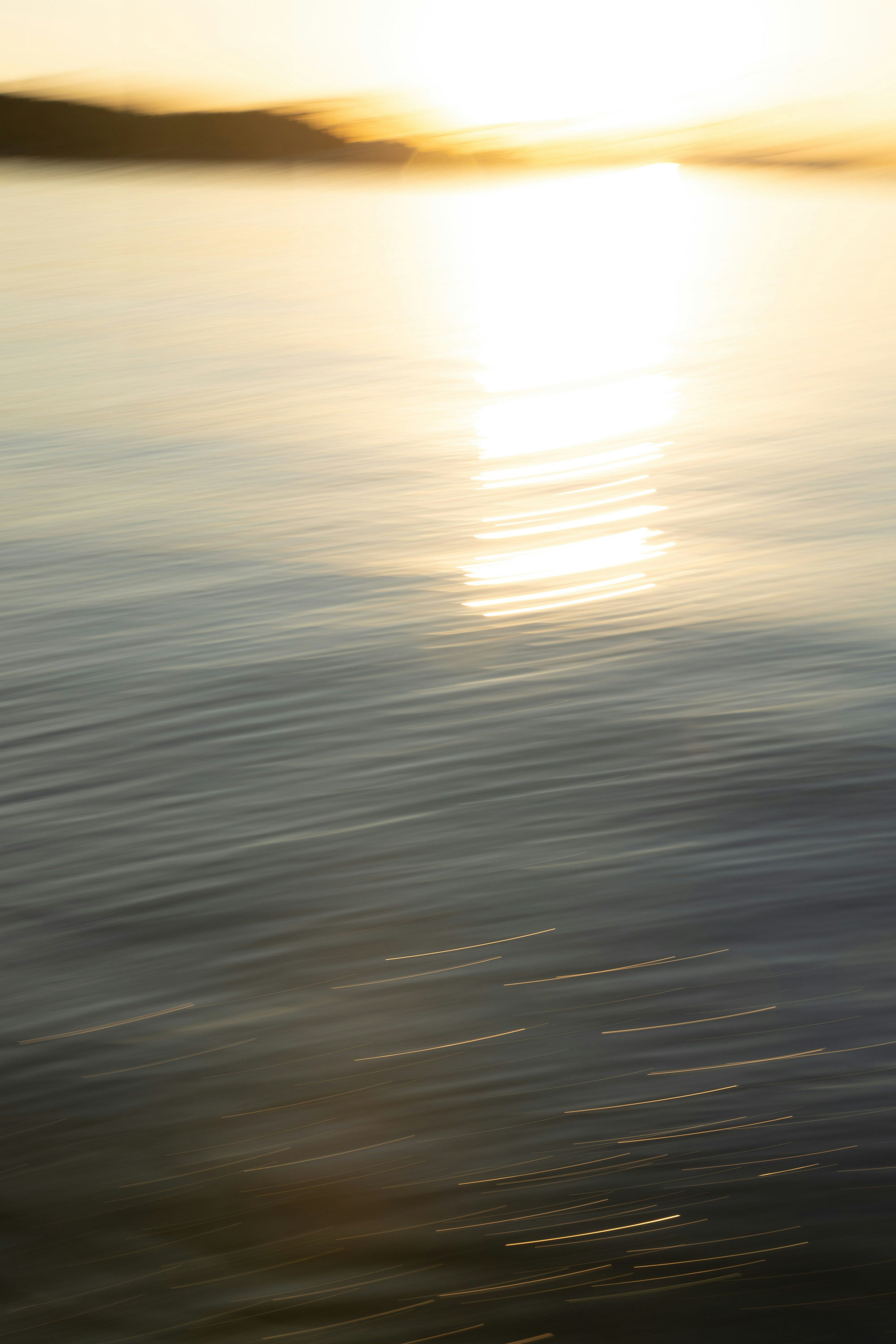 水面に反射する夕日の柔らかい光と穏やかな波の動き