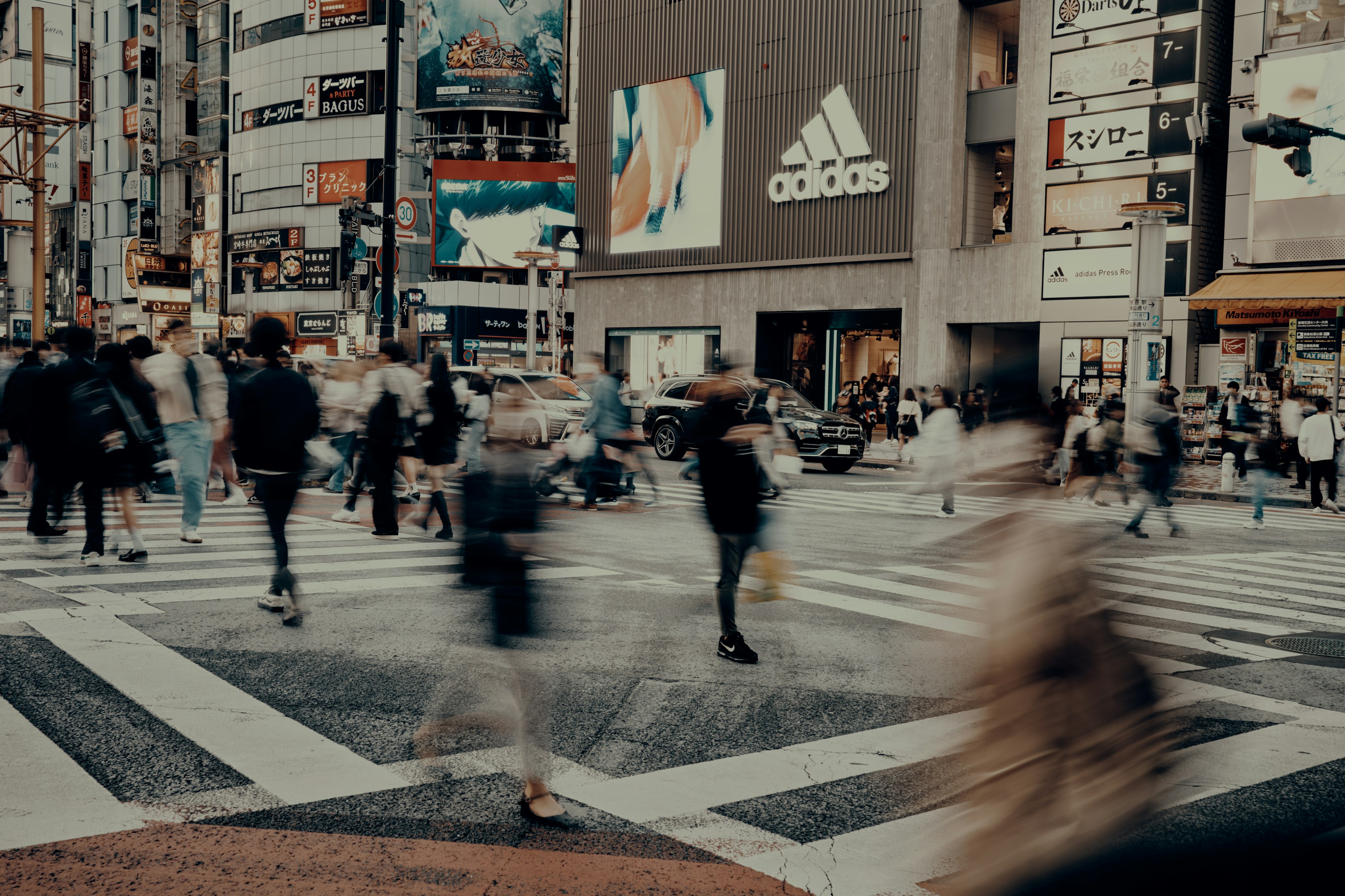 Cruce peatonal concurrido con personas y un anuncio de Adidas al fondo