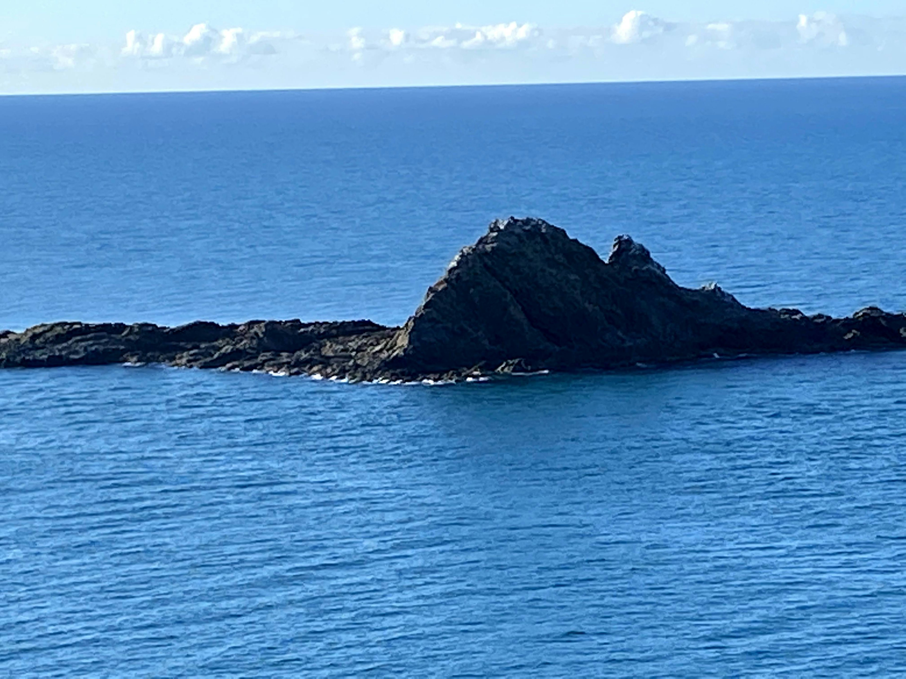 Felsige Insel, die aus dem lebhaften blauen Ozean auftaucht