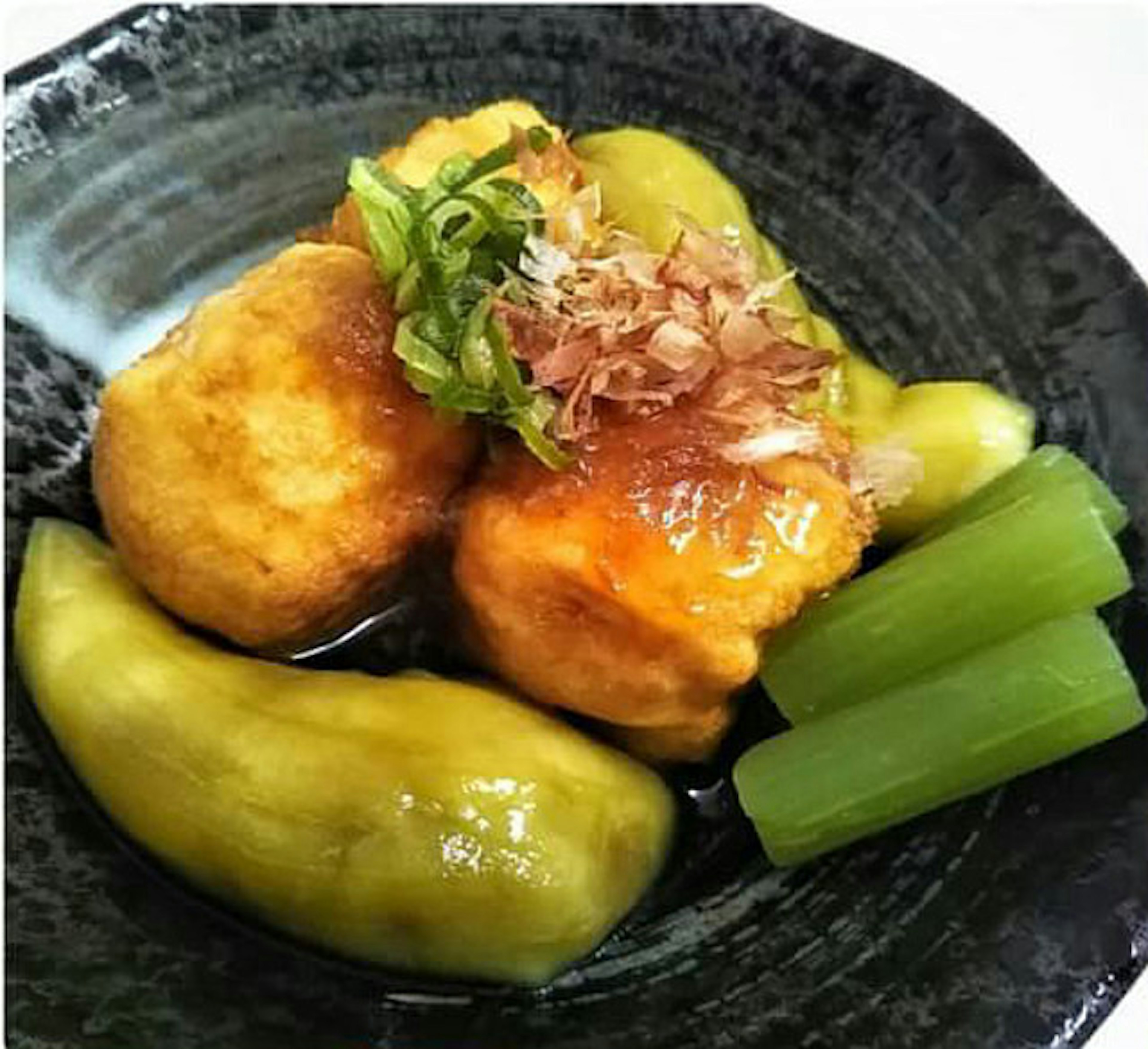 Fried tofu served with green vegetables on a black plate