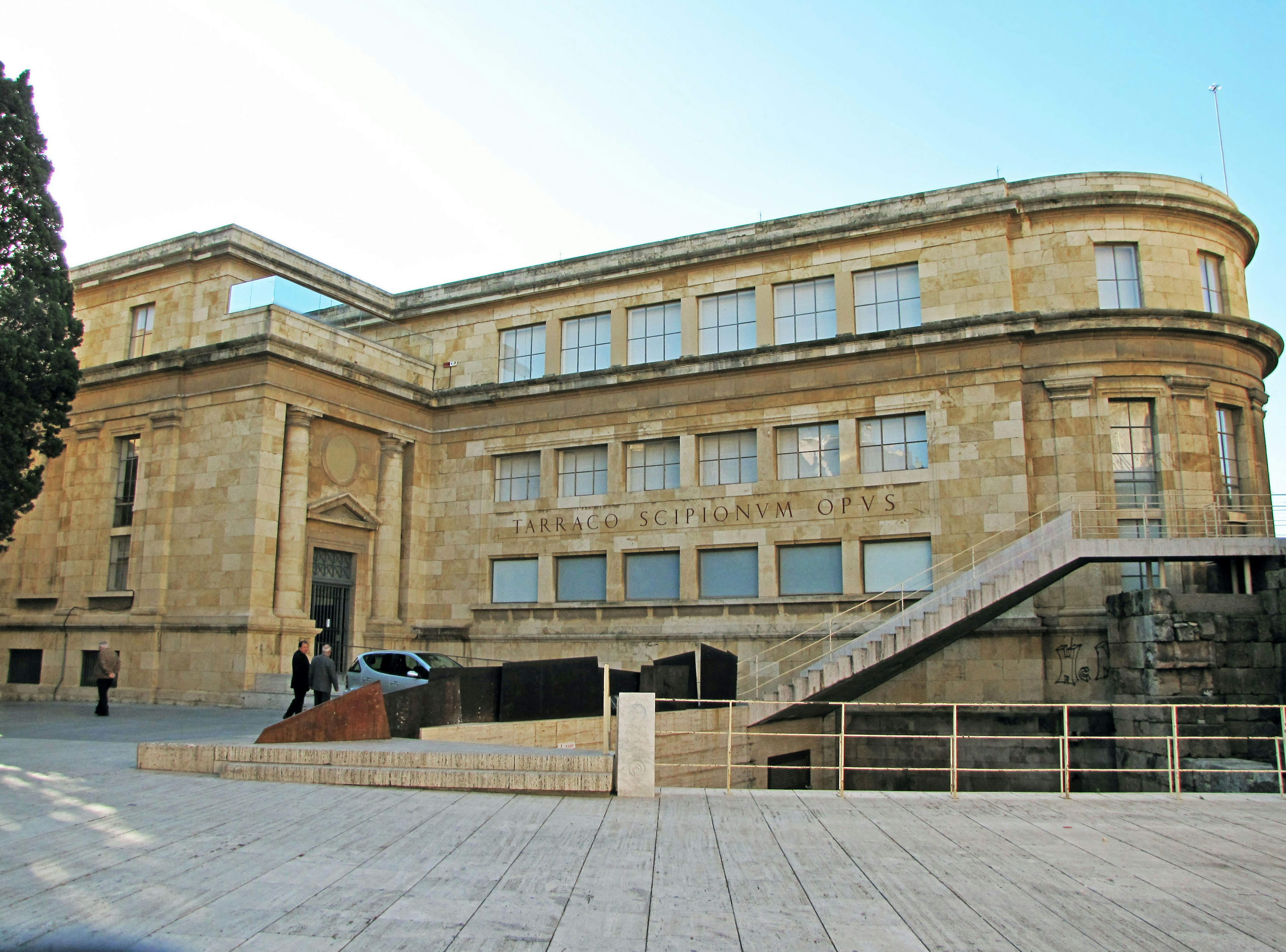 Exterior of an art museum, bright sky, stone facade, stairs and modern sculpture