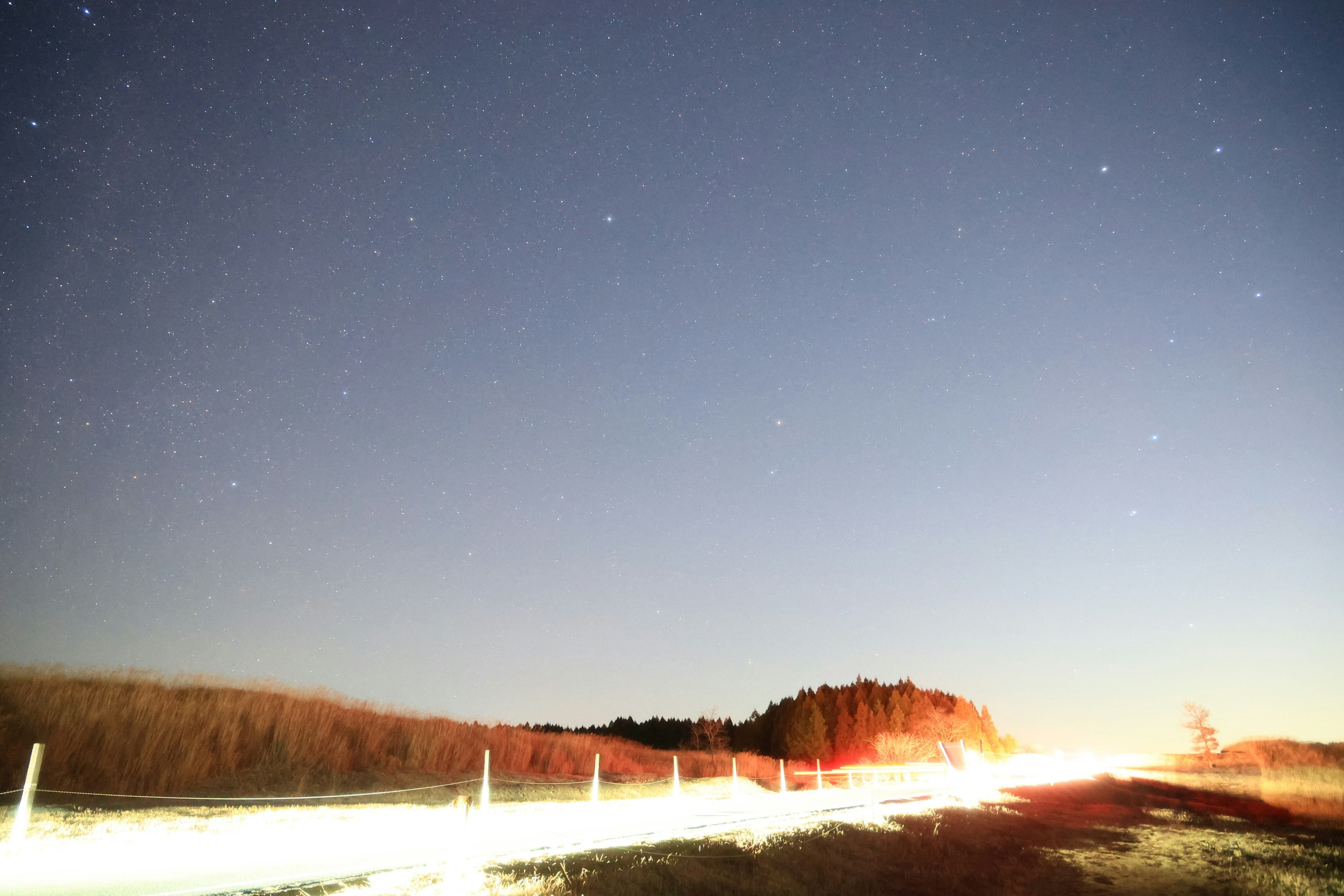 Nachtszene mit sternenklarem Himmel und Lichtspuren auf einer Straße