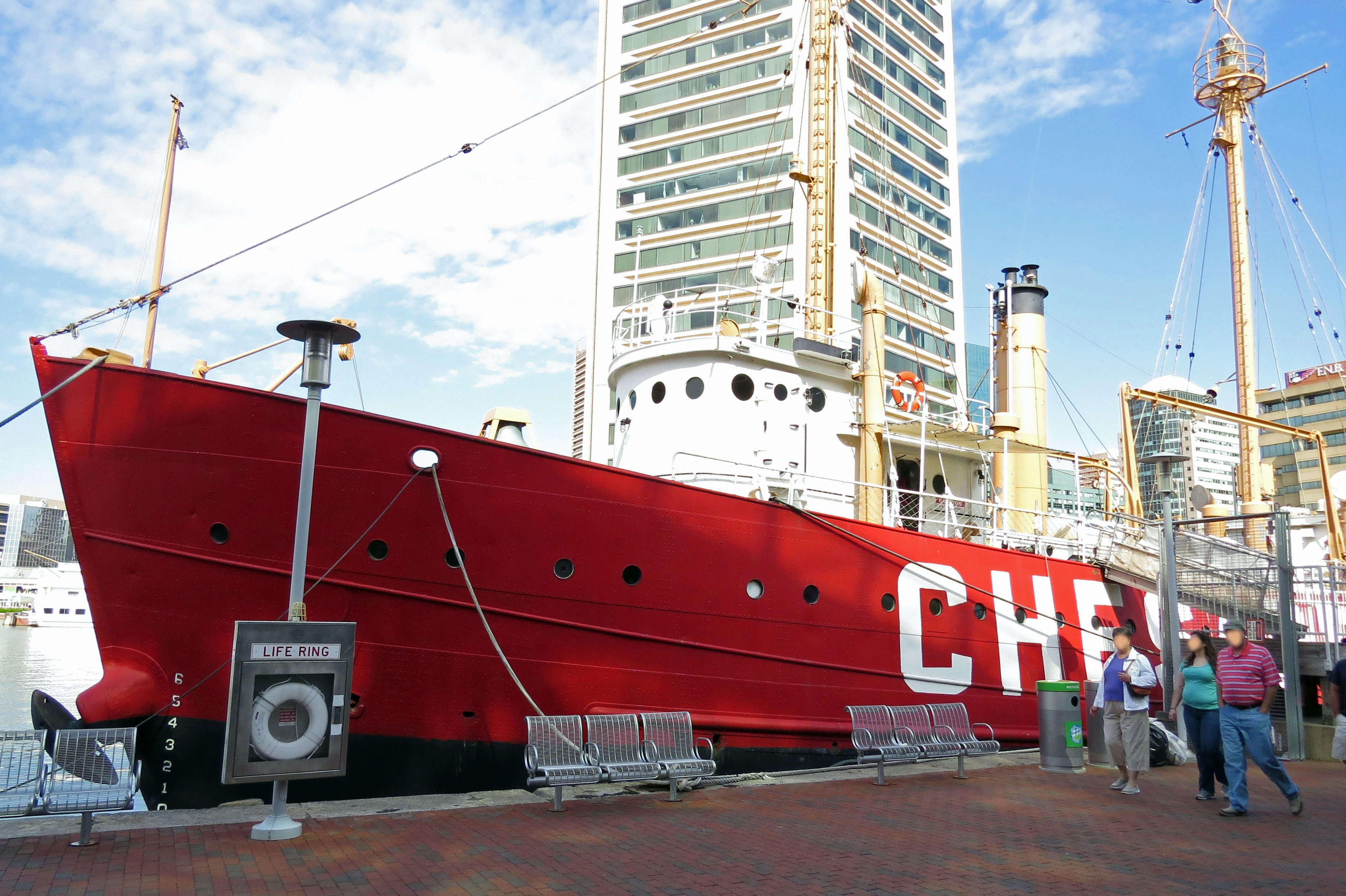 Un bateau rouge amarré au port avec des bâtiments environnants et des personnes