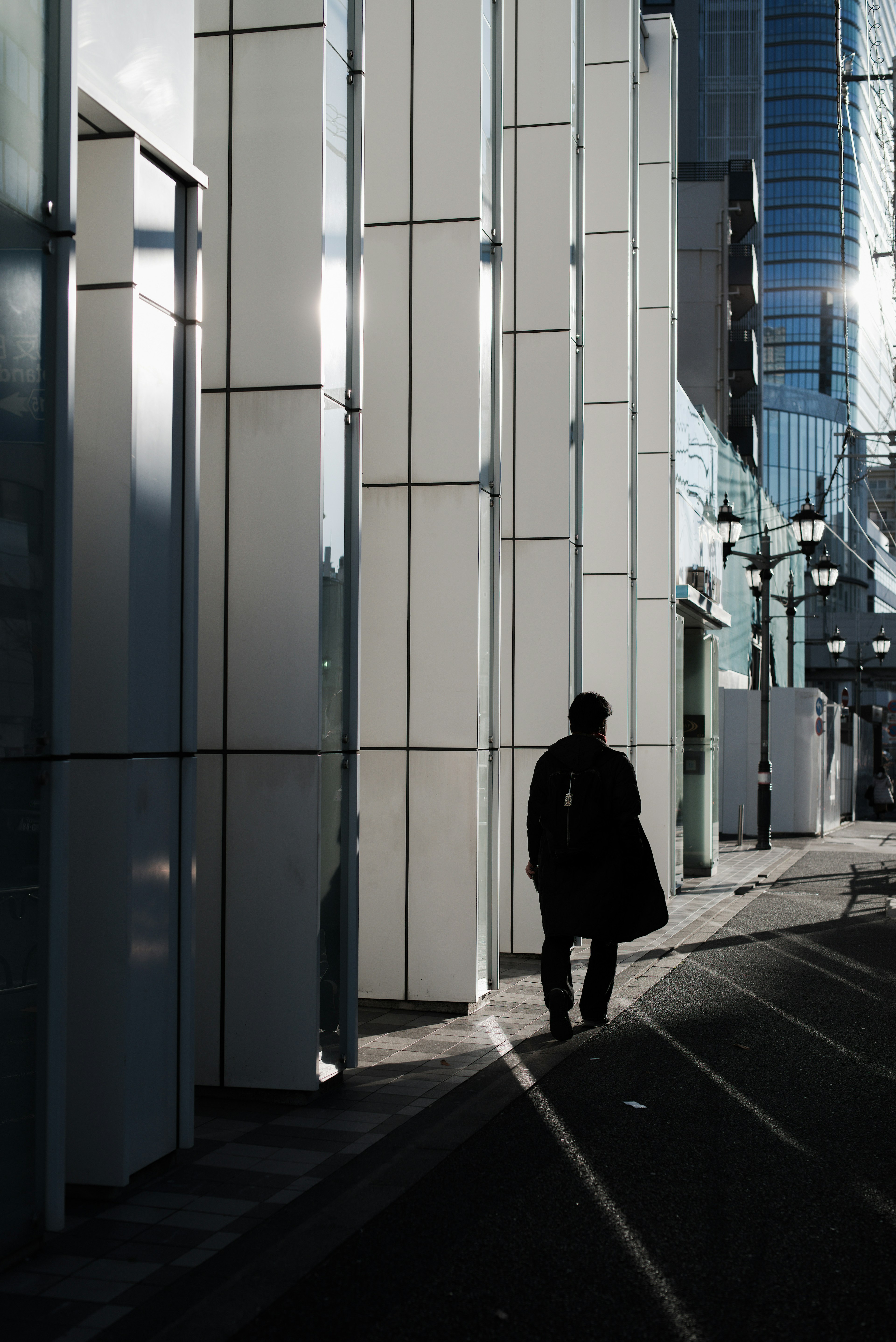 Silhouette de una persona caminando junto a edificios modernos que reflejan luz