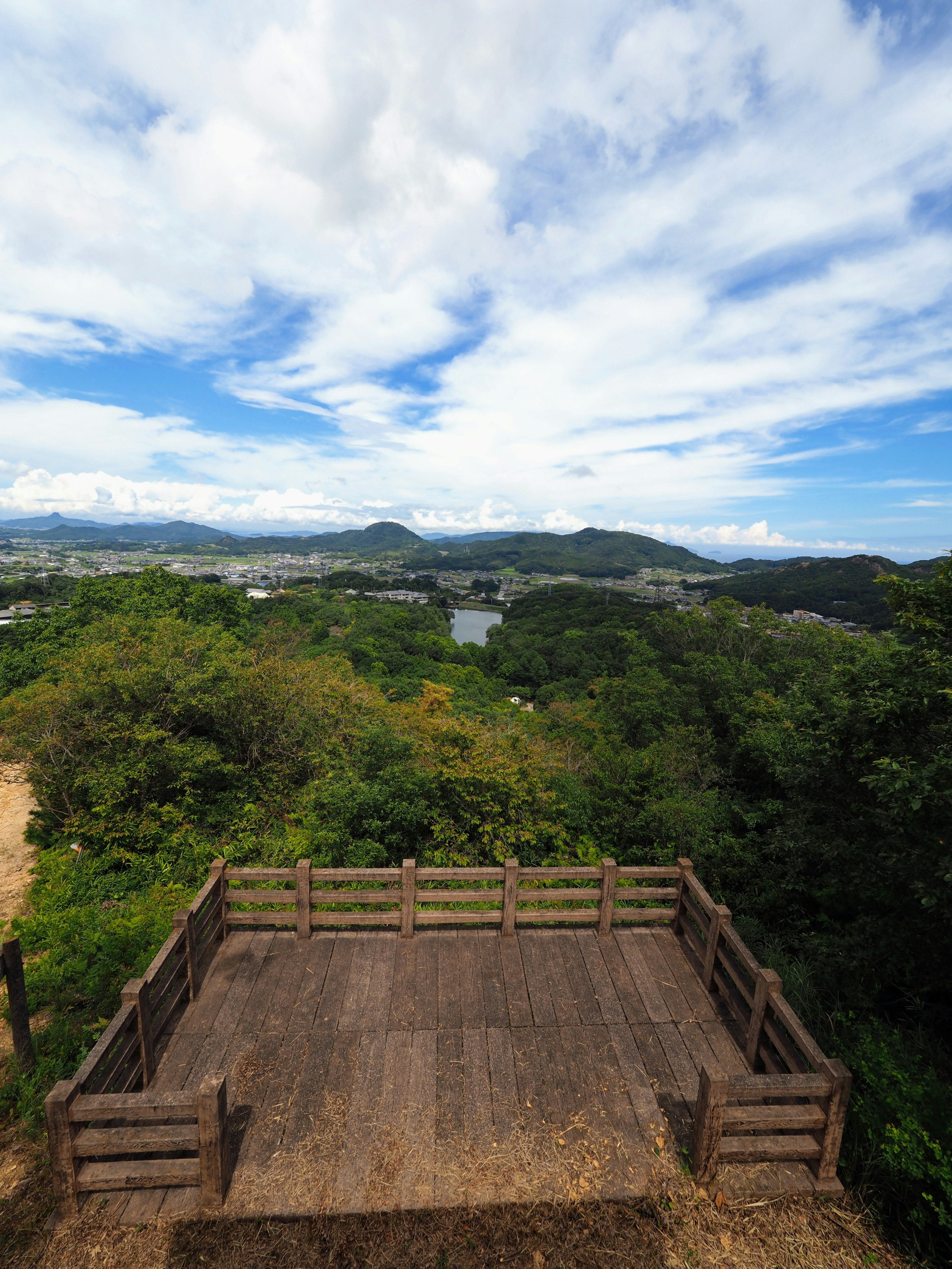 Scenic view from a wooden observation deck surrounded by greenery blue sky with clouds