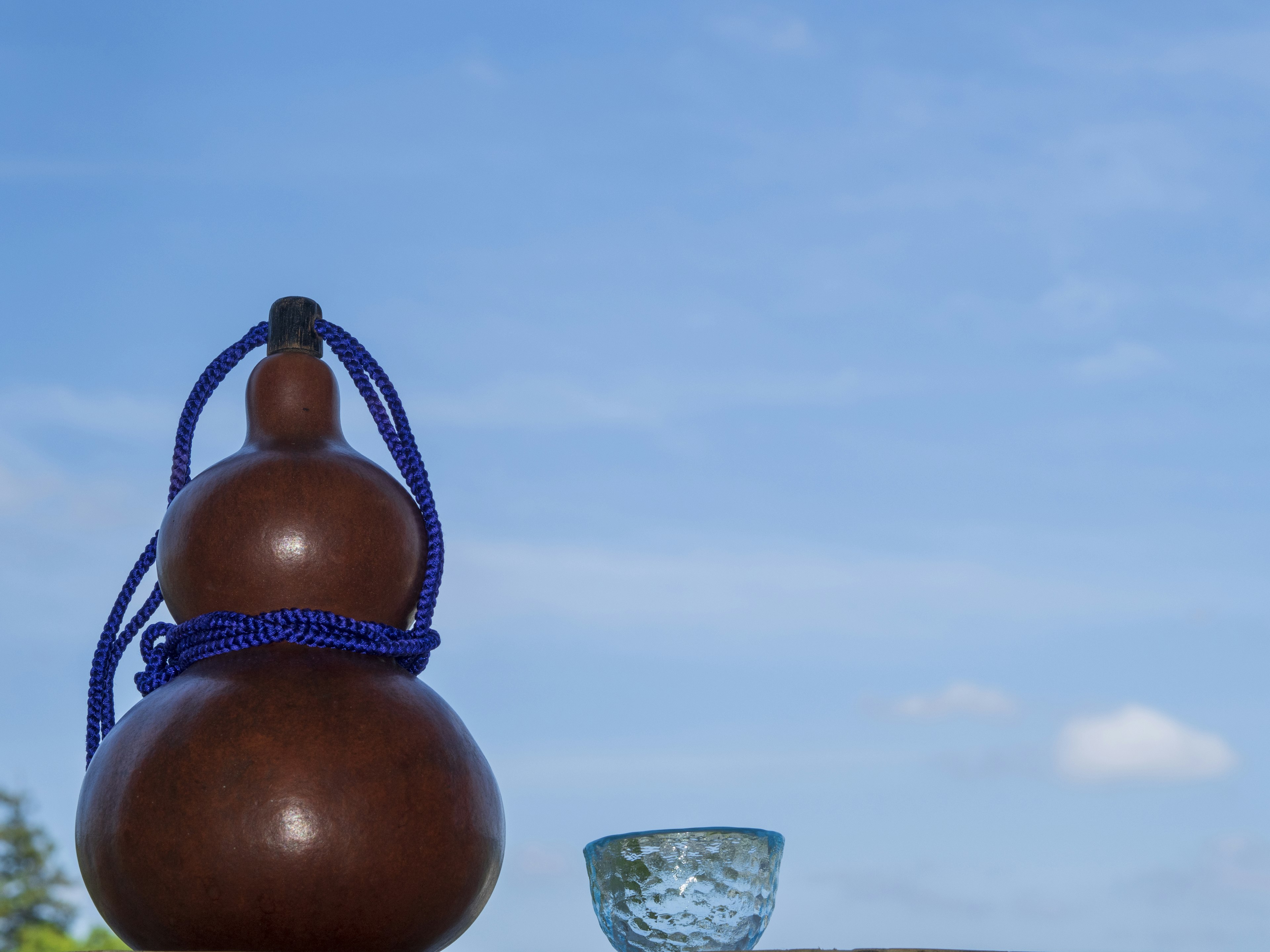 A brown gourd with a blue cord and a clear glass bowl under a blue sky