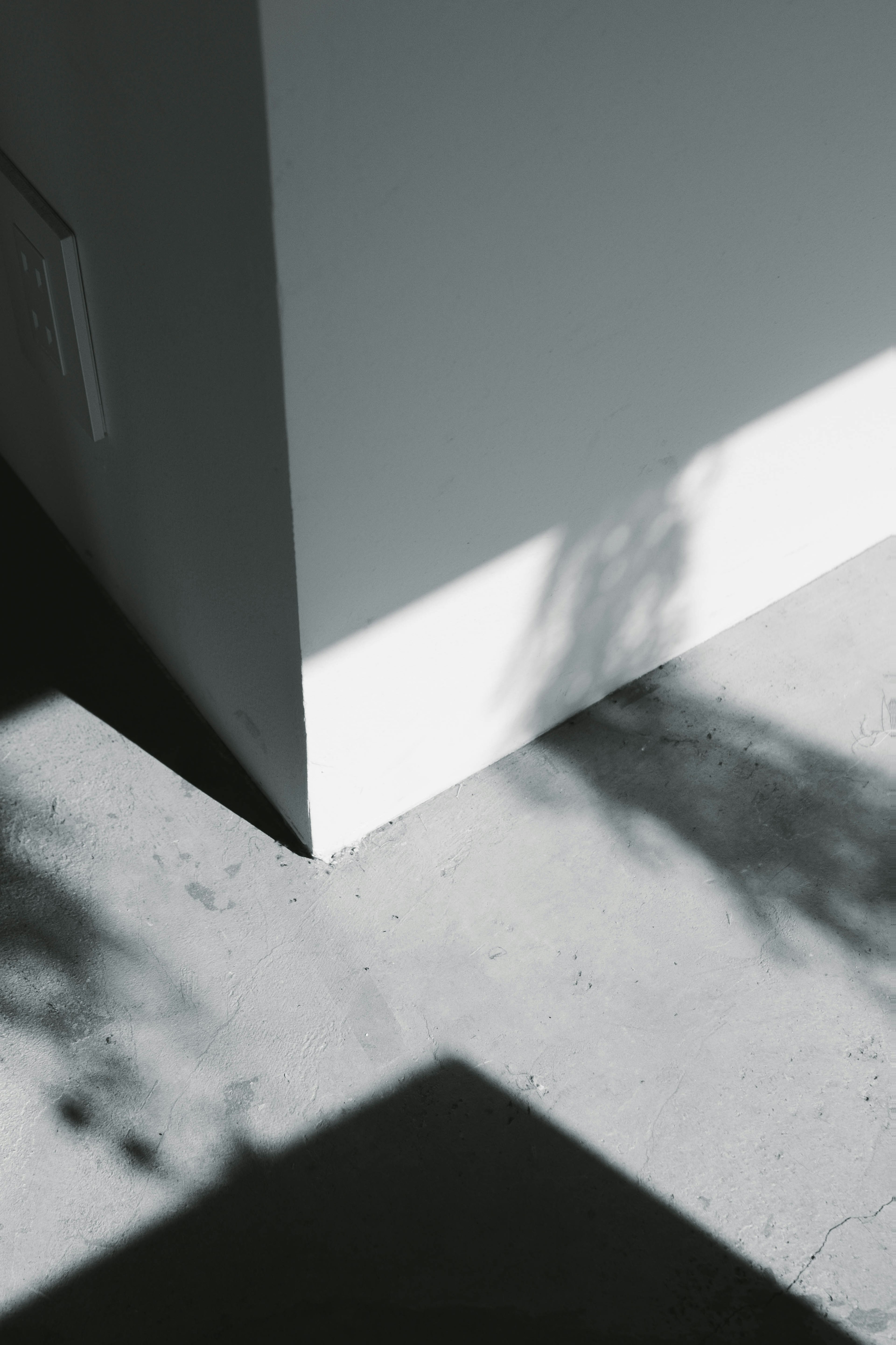 Coin d'un mur blanc avec des ombres contrastantes sur un sol en béton