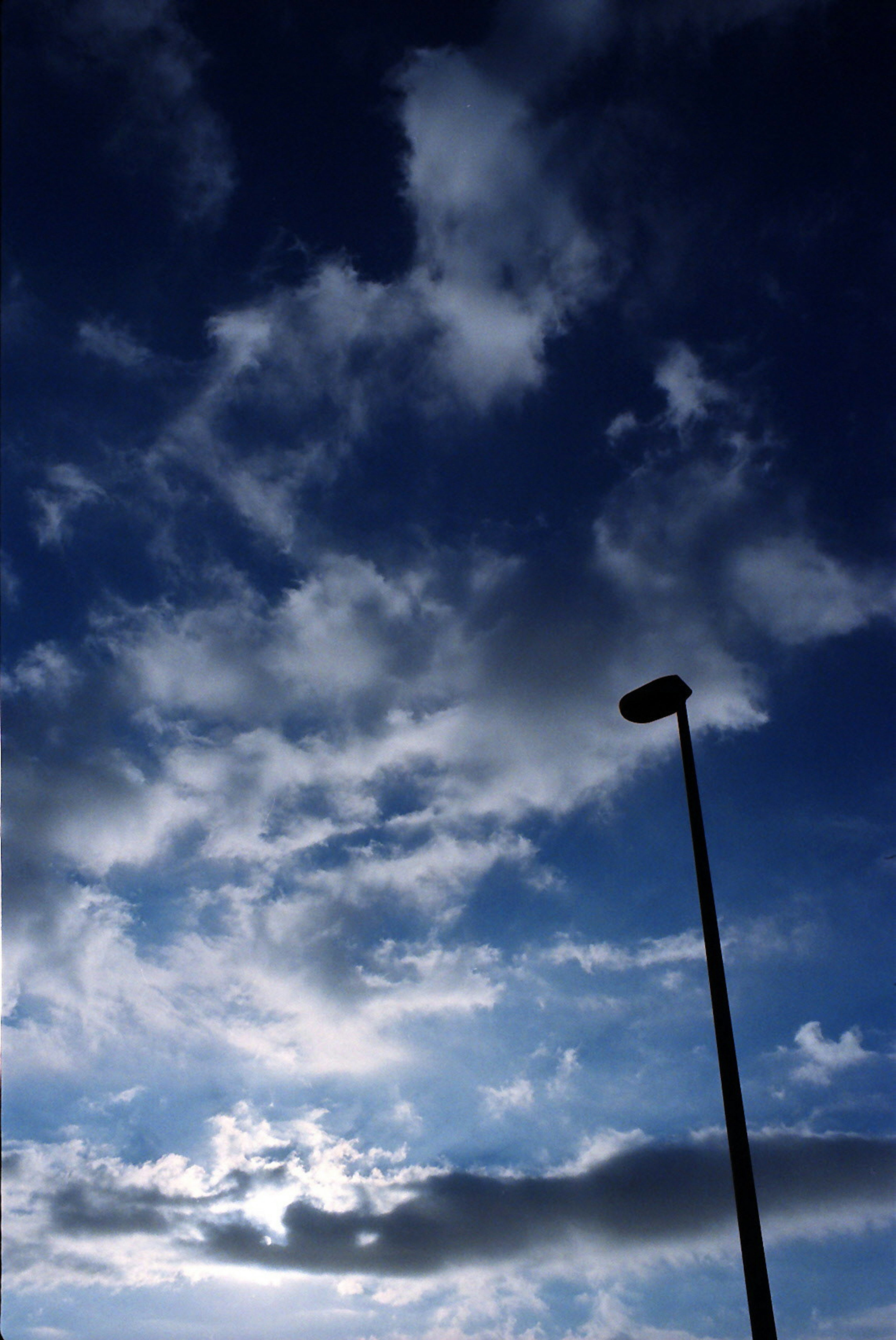 Silueta de una farola contra un cielo azul con nubes blancas