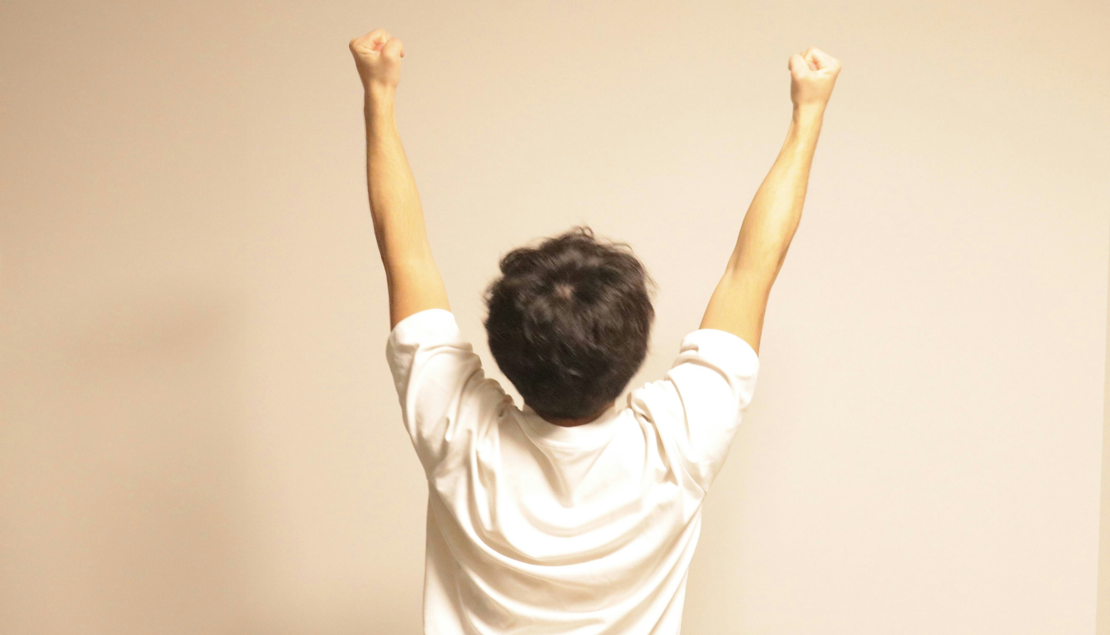 A man in a white shirt raising both arms in celebration from behind