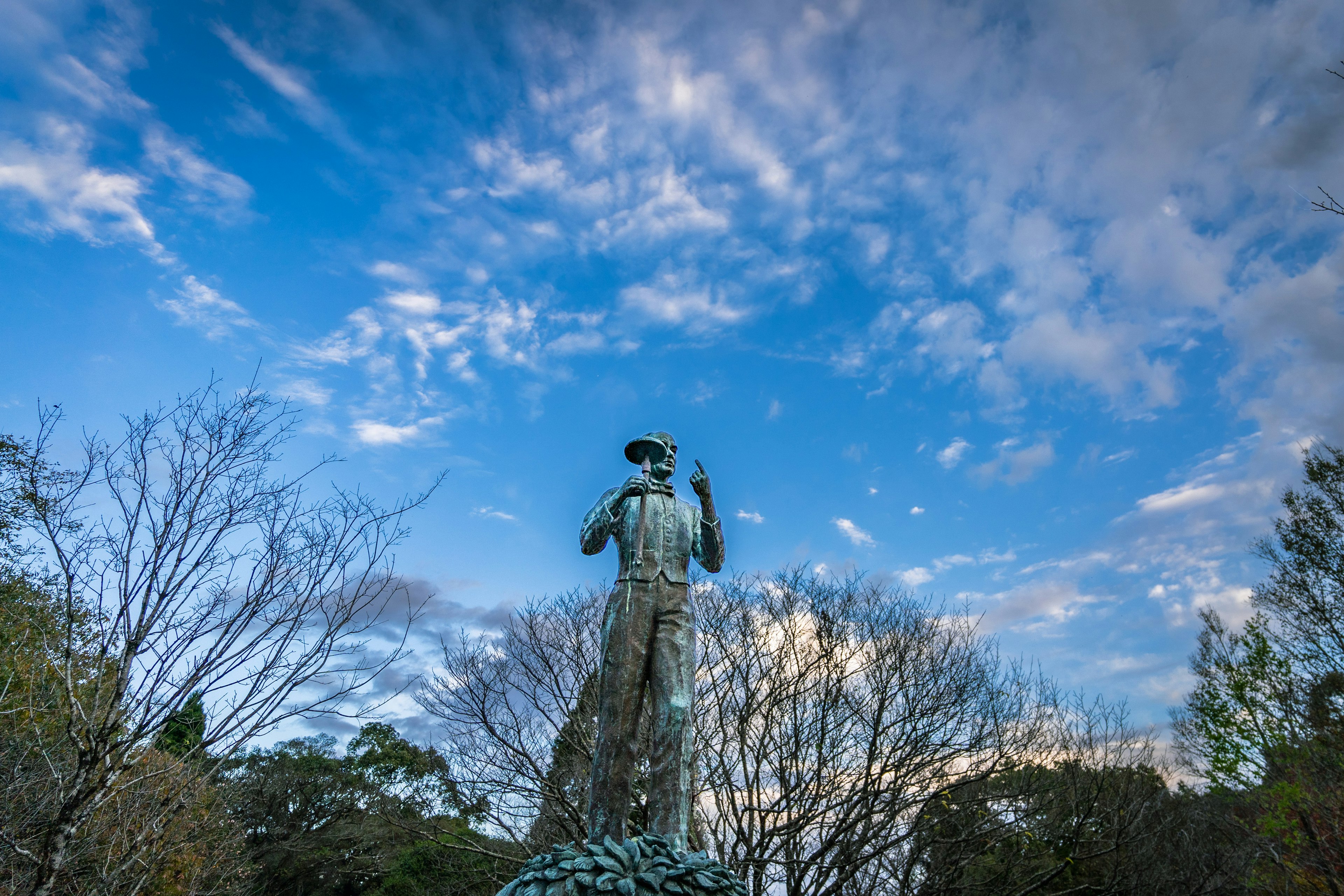 Estatua de pie bajo un cielo azul con nubes y árboles