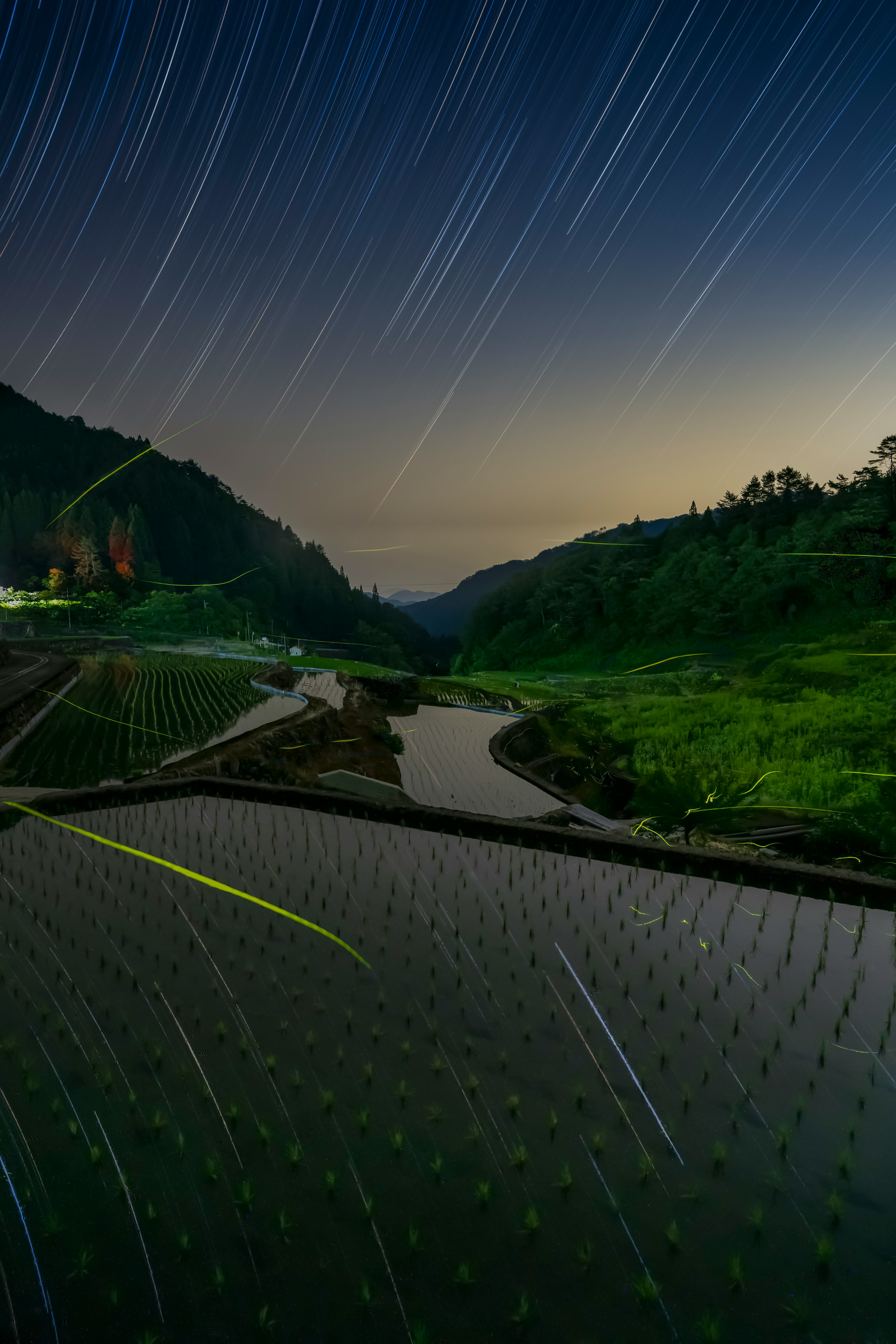 星の軌跡が見える夜空の下の川と山の風景